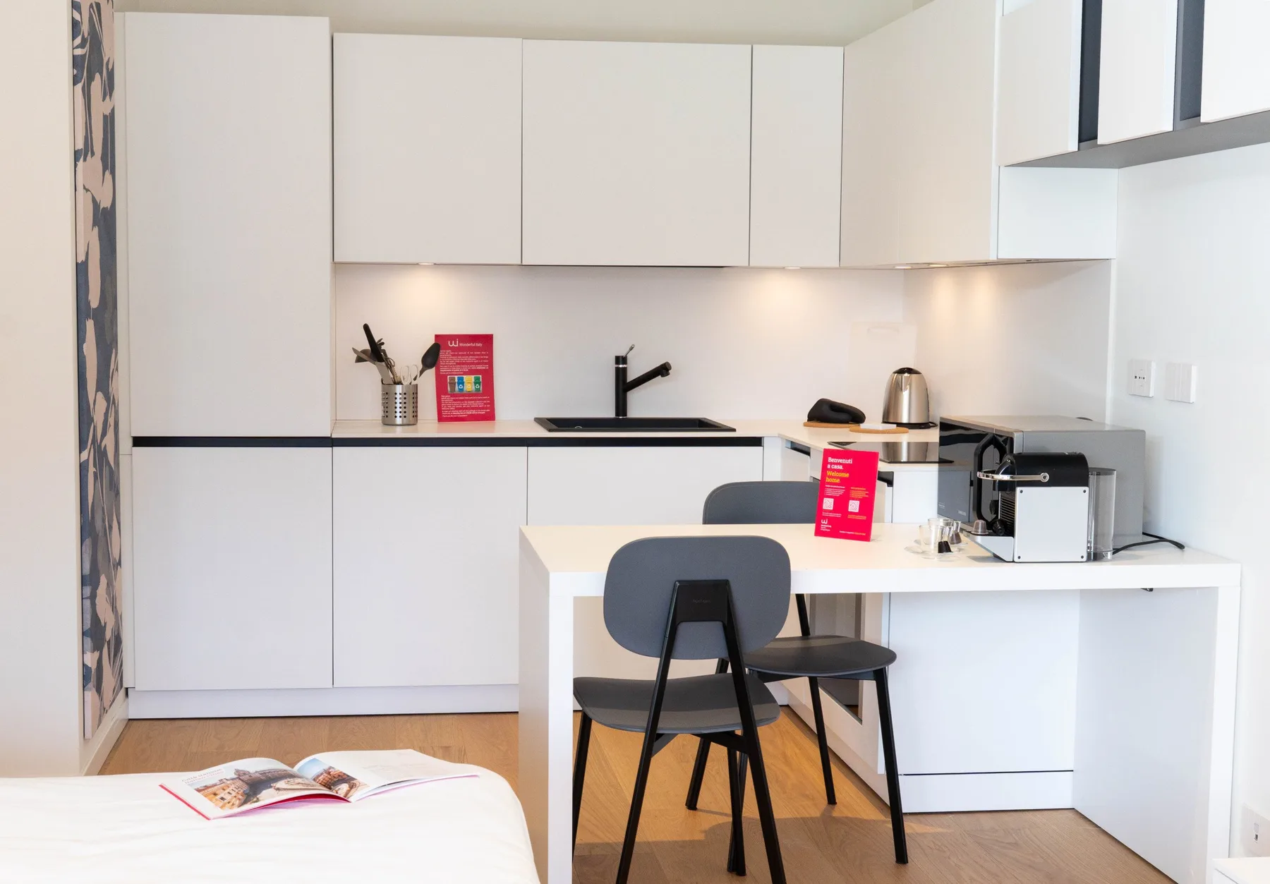 A bright kitchenette with white cabinets, a counter, and a small dining table.