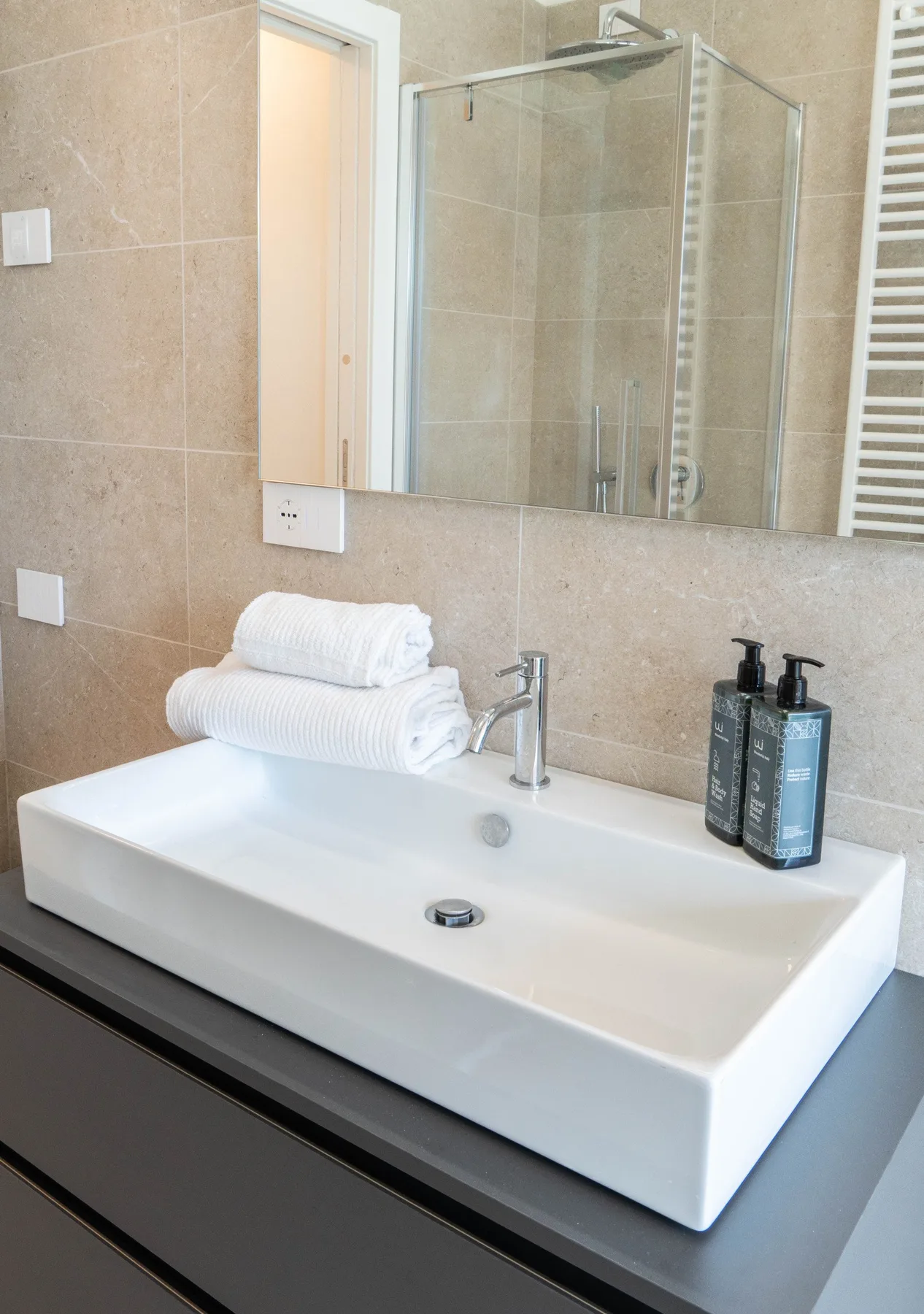 A bathroom vanity with a wide white sink, folded towels, and a wall mirror.