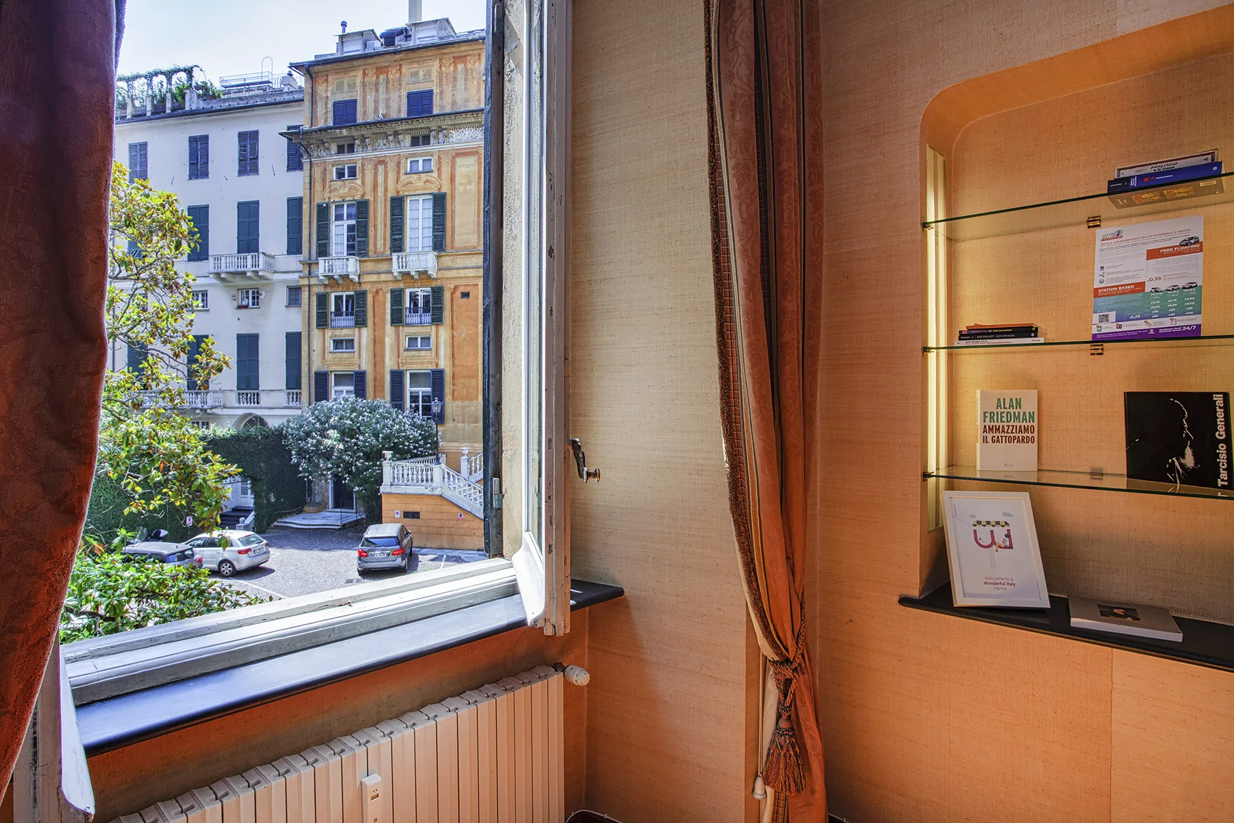A room with an open window overlooking nearby buildings and a display shelf.