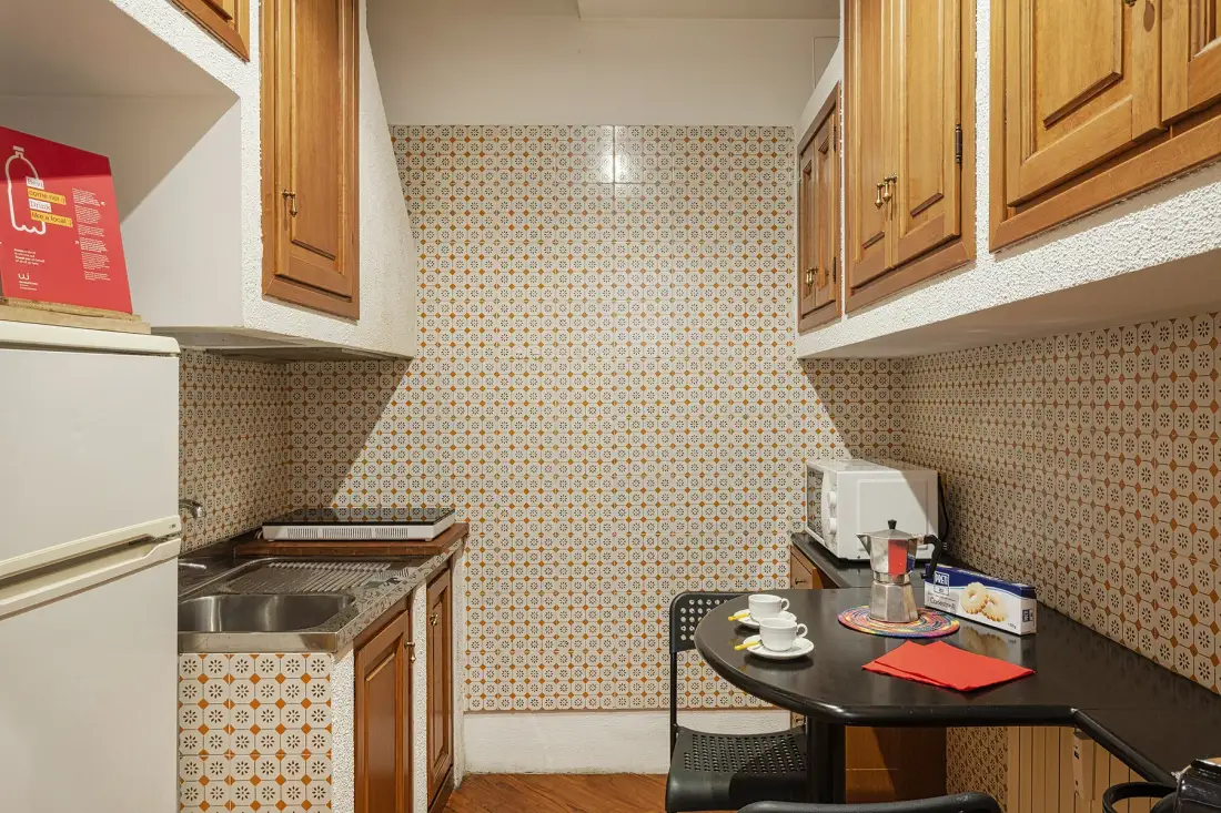 Una cocina compacta con azulejos estampados, armarios de madera y una mesa pequeña.