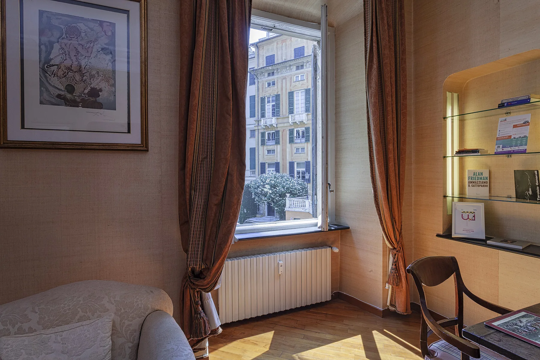 A bedroom with a tall window, curtains, and a view of a nearby building.