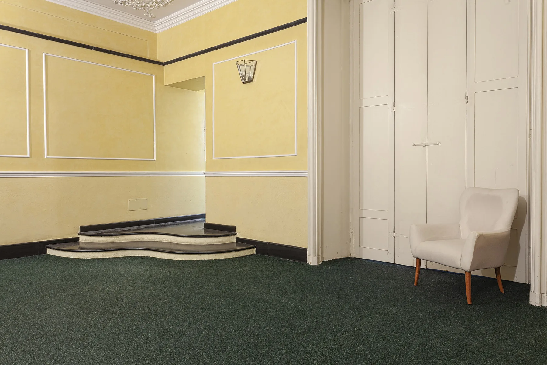 Una sala formal con paredes claras paneladas y un asiento tapizado.