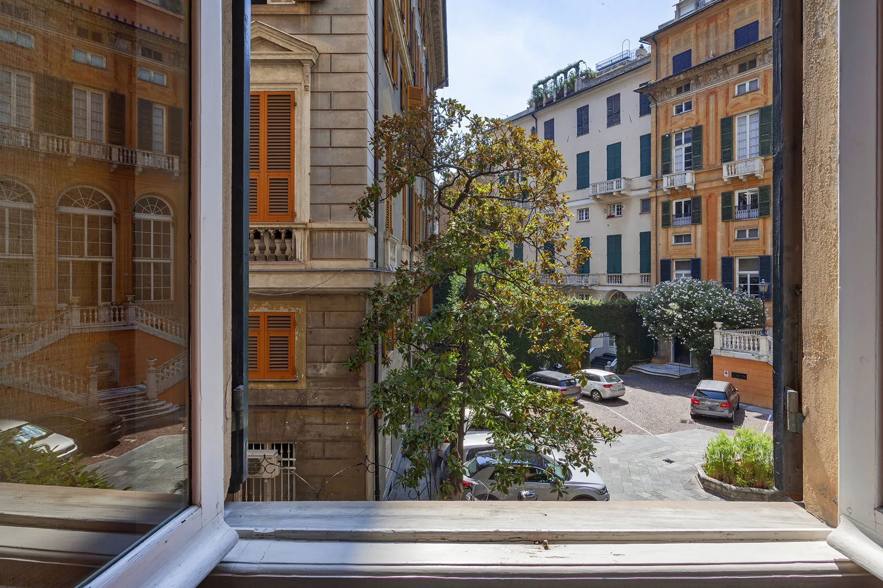 Un patio visto a través de una ventana abierta, con árboles y edificios alrededor.