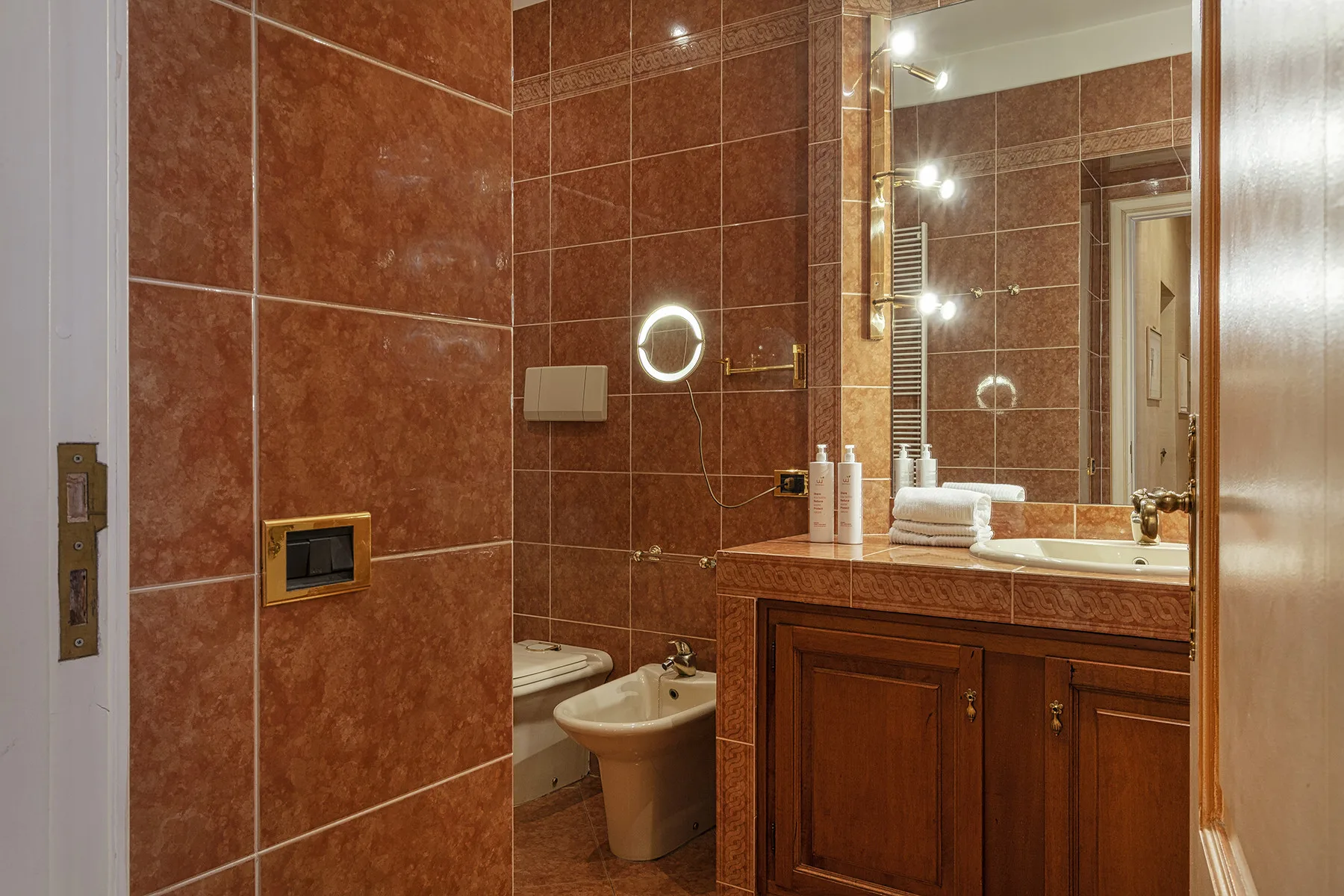 Un baño con azulejos, lavabo con mueble de madera y un espejo grande.