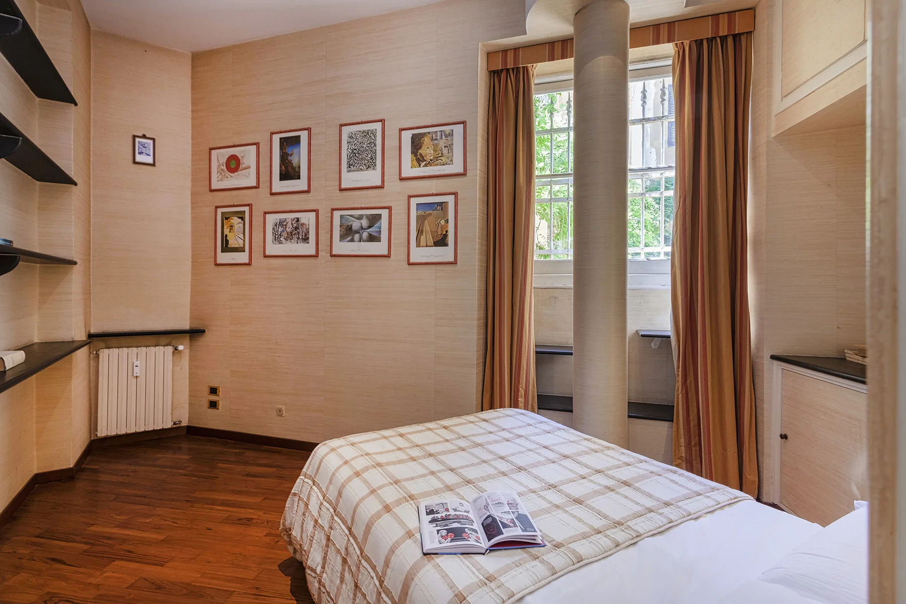 Un dormitorio con una cama, cuadros enmarcados y una ventana con cortinas.