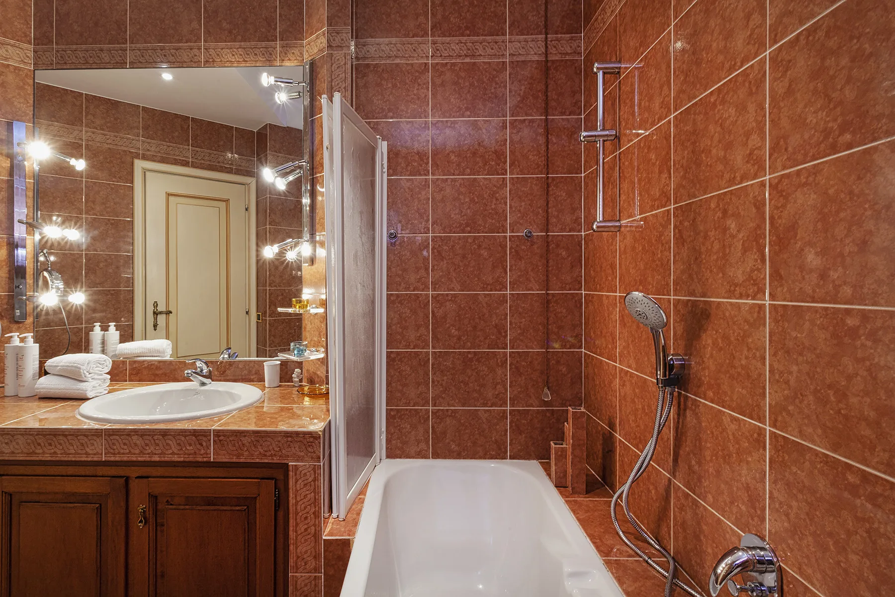 Un baño alicatado con bañera, ducha y lavabo junto a un espejo grande.
