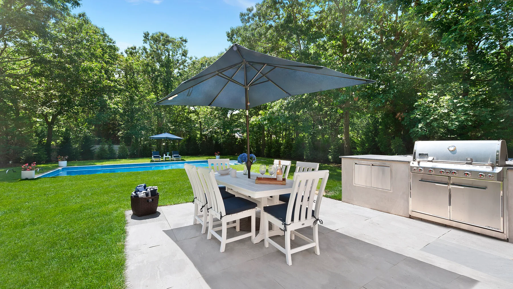 Una zona de comedor al aire libre con una sombrilla grande junto a una piscina.