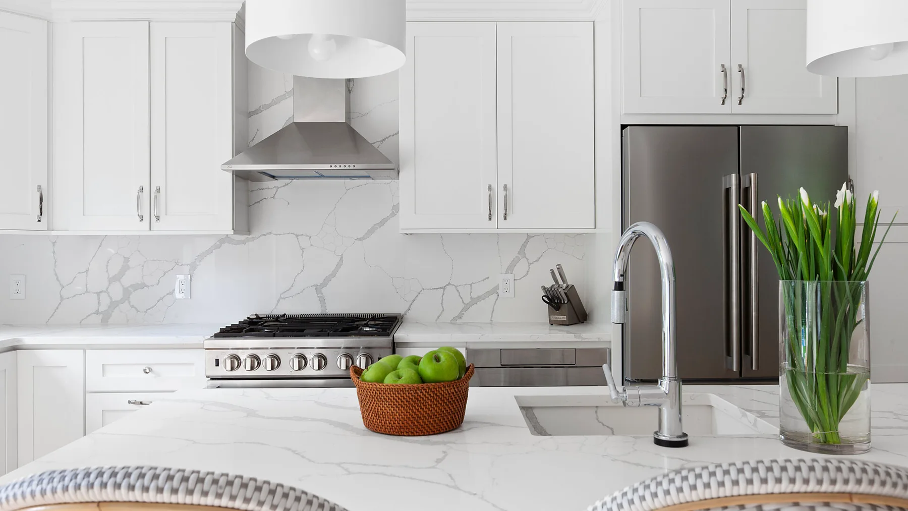 Una cocina blanca y luminosa con una isla de efecto mármol y electrodomésticos de acero inoxidable.