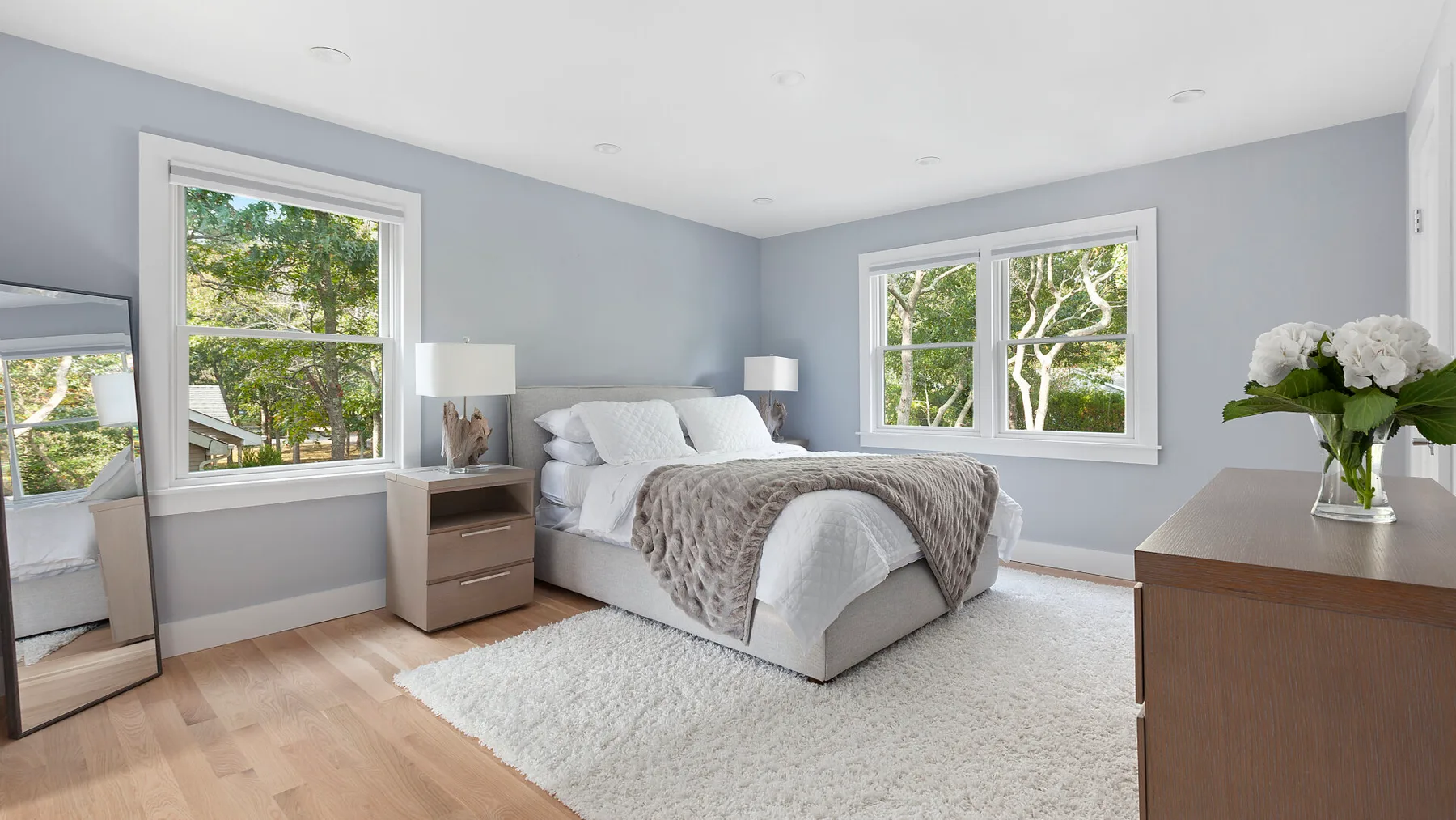 Un dormitorio luminoso con una cama, paredes claras y ventanas grandes.