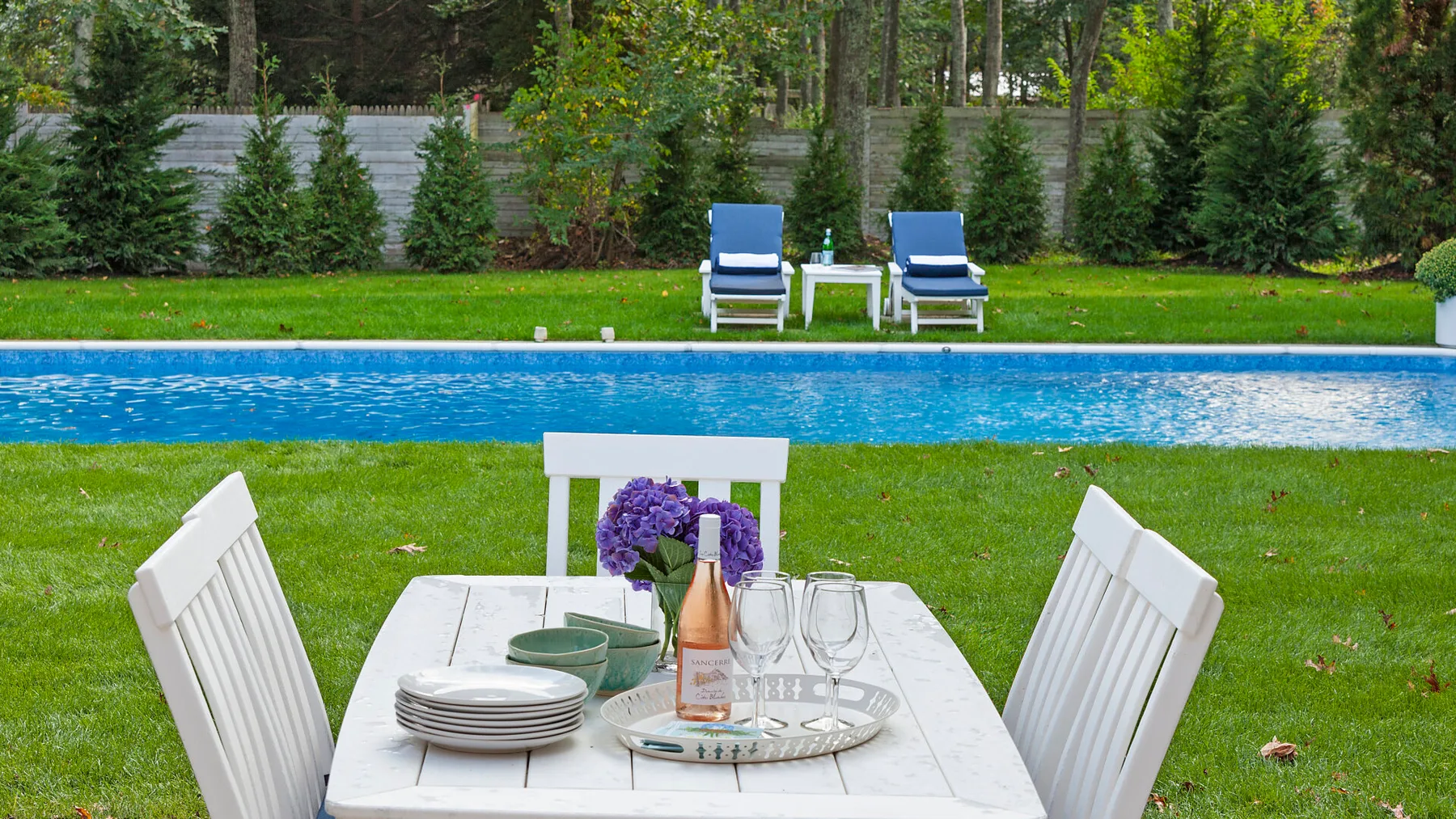 Una mesa y asientos al aire libre dan a una piscina y un césped verde.