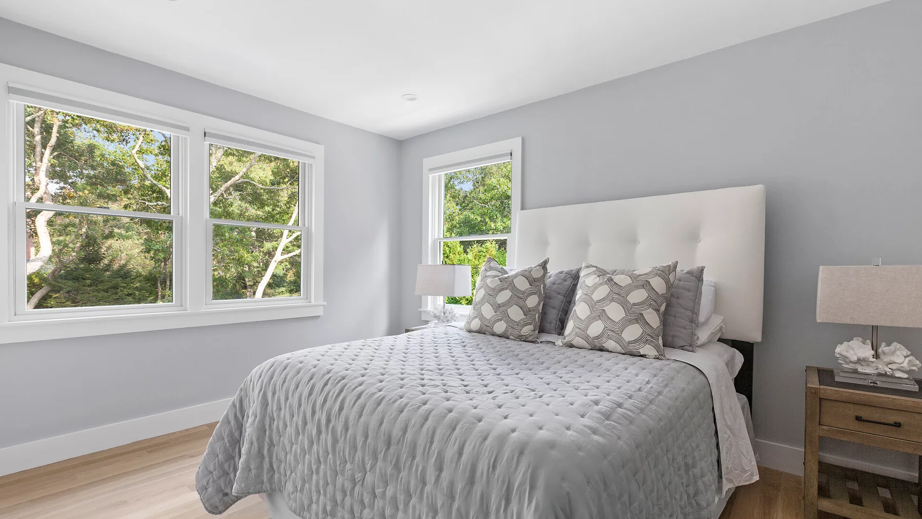 Un dormitorio luminoso con una cama grande, almohadas estampadas y ventanas con vista a los árboles.