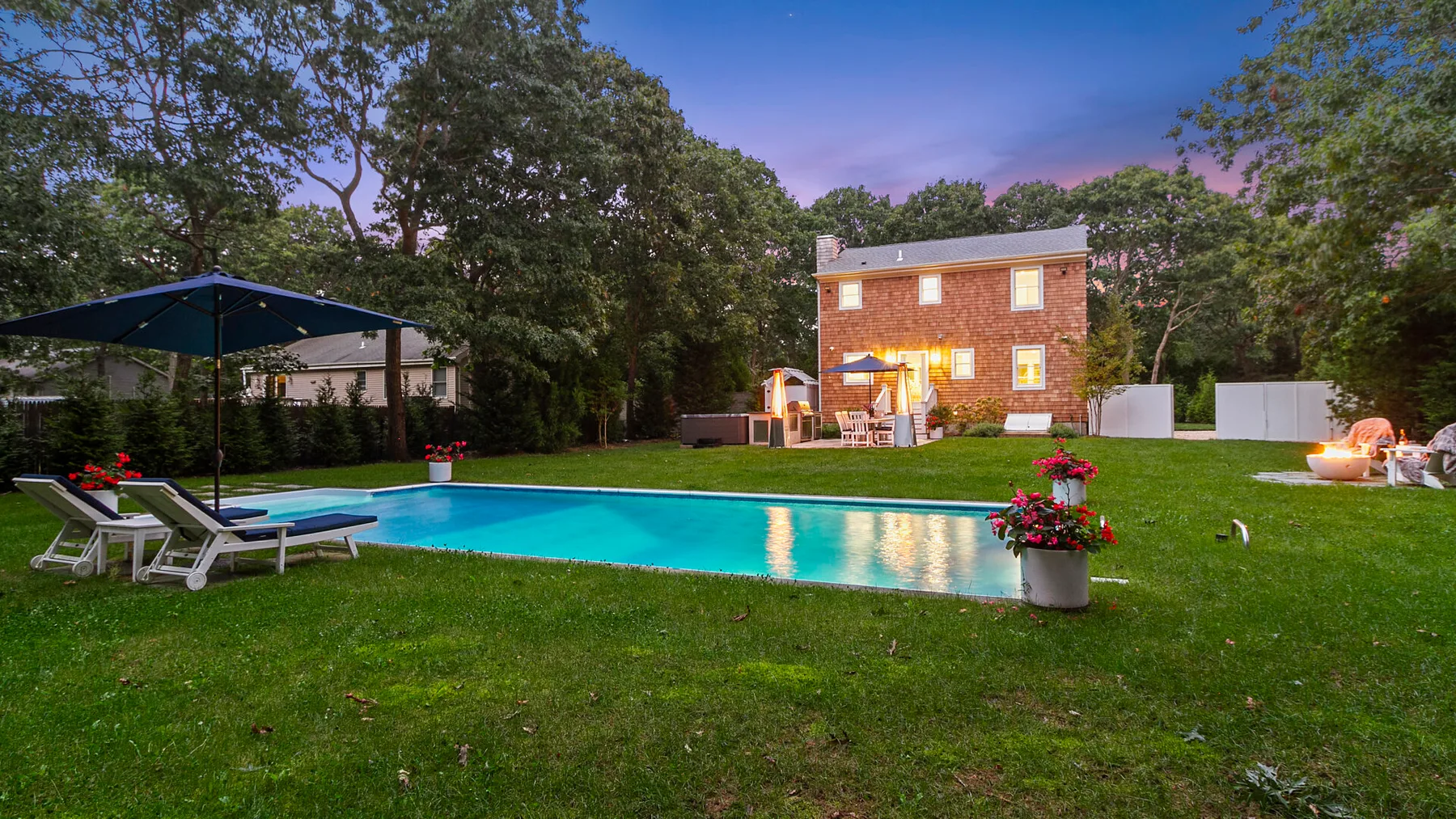 Una piscina al aire libre está junto a un césped, una casa de ladrillo y asientos de patio.