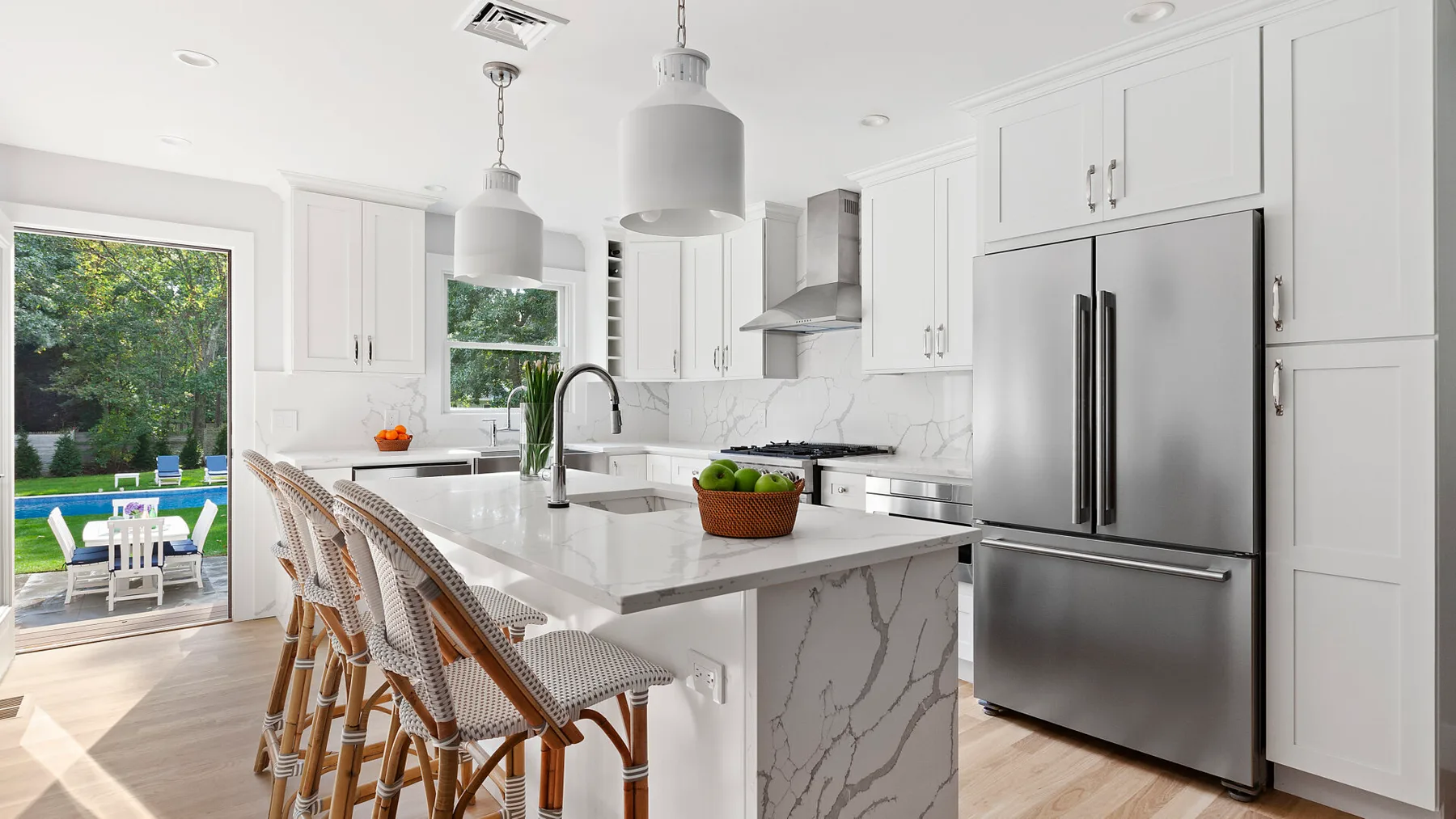 Una cocina blanca y luminosa con isla de mármol, asientos de barra y electrodomésticos de acero inoxidable.