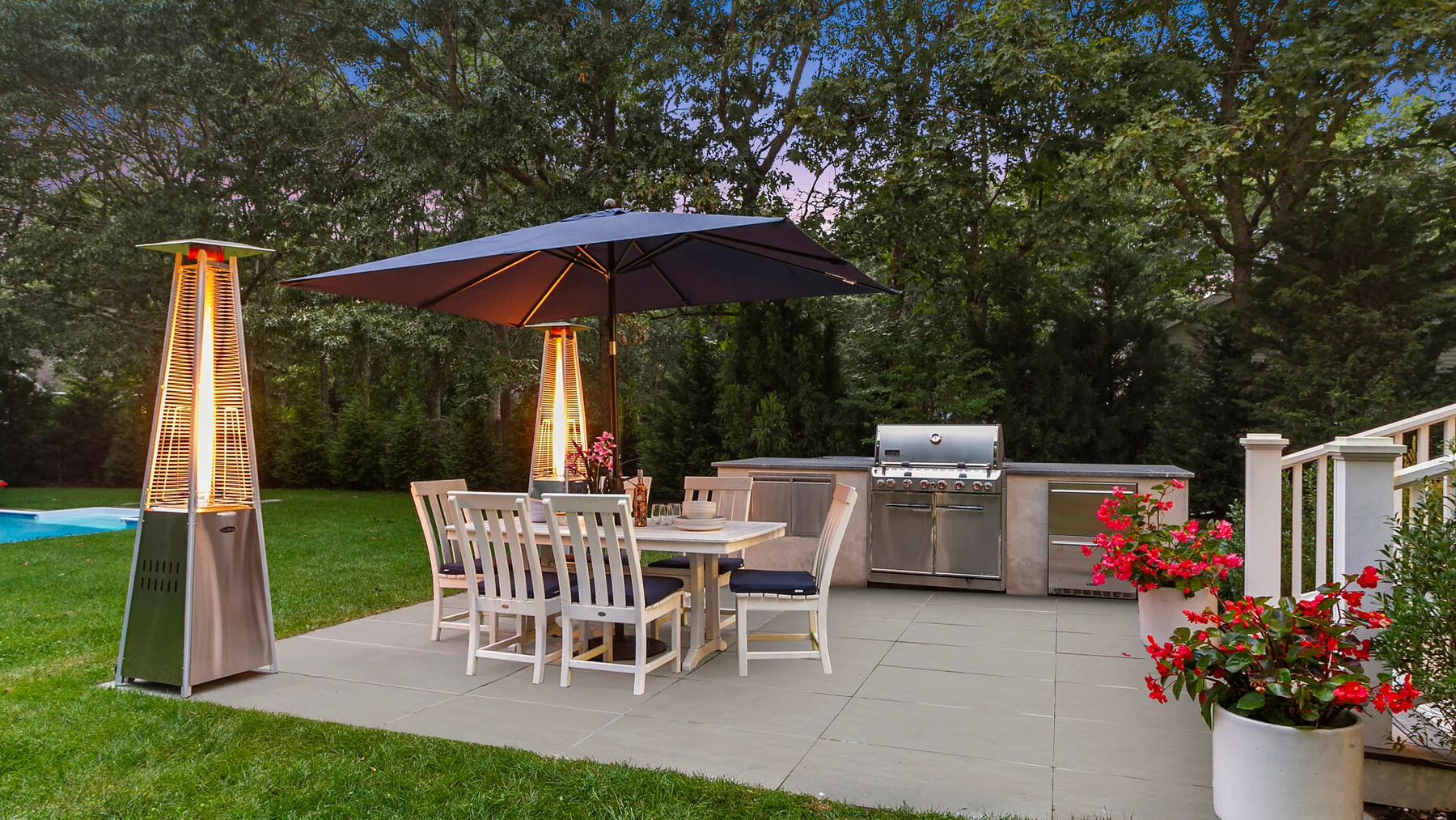 Un comedor al aire libre en un patio, con una sombrilla grande y una cocina exterior.