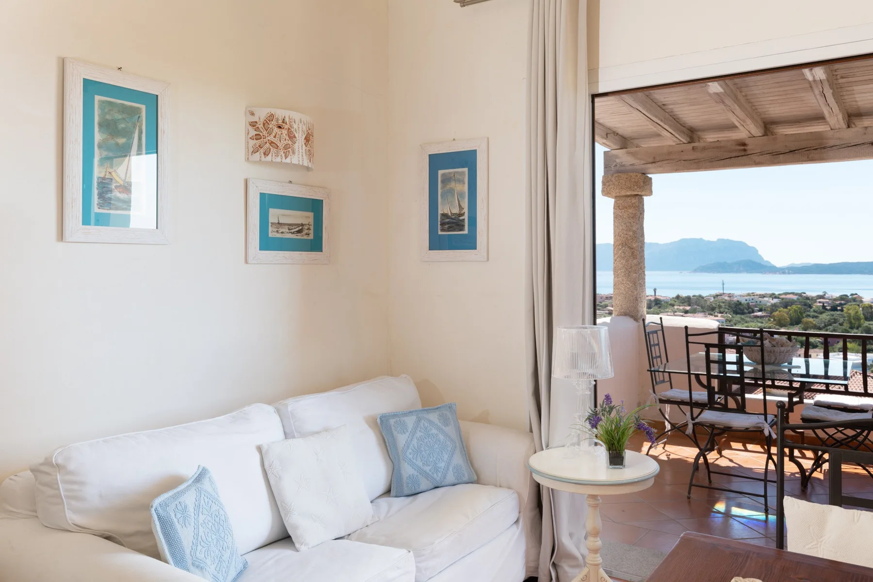 A bright living area opens onto a covered terrace with seating and a distant coastal view.
