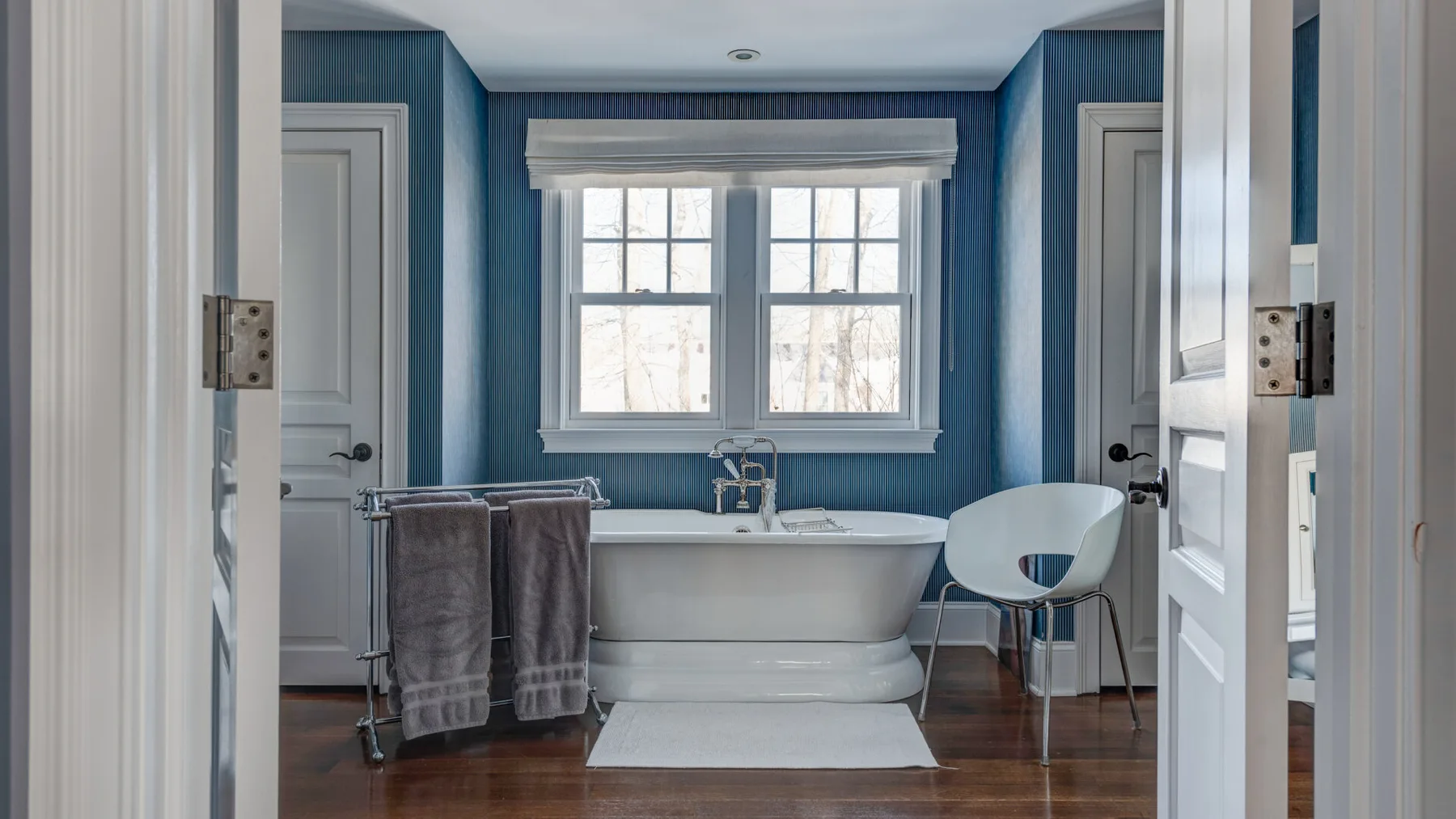 Un baño con una bañera independiente bajo una ventana y paredes azules.