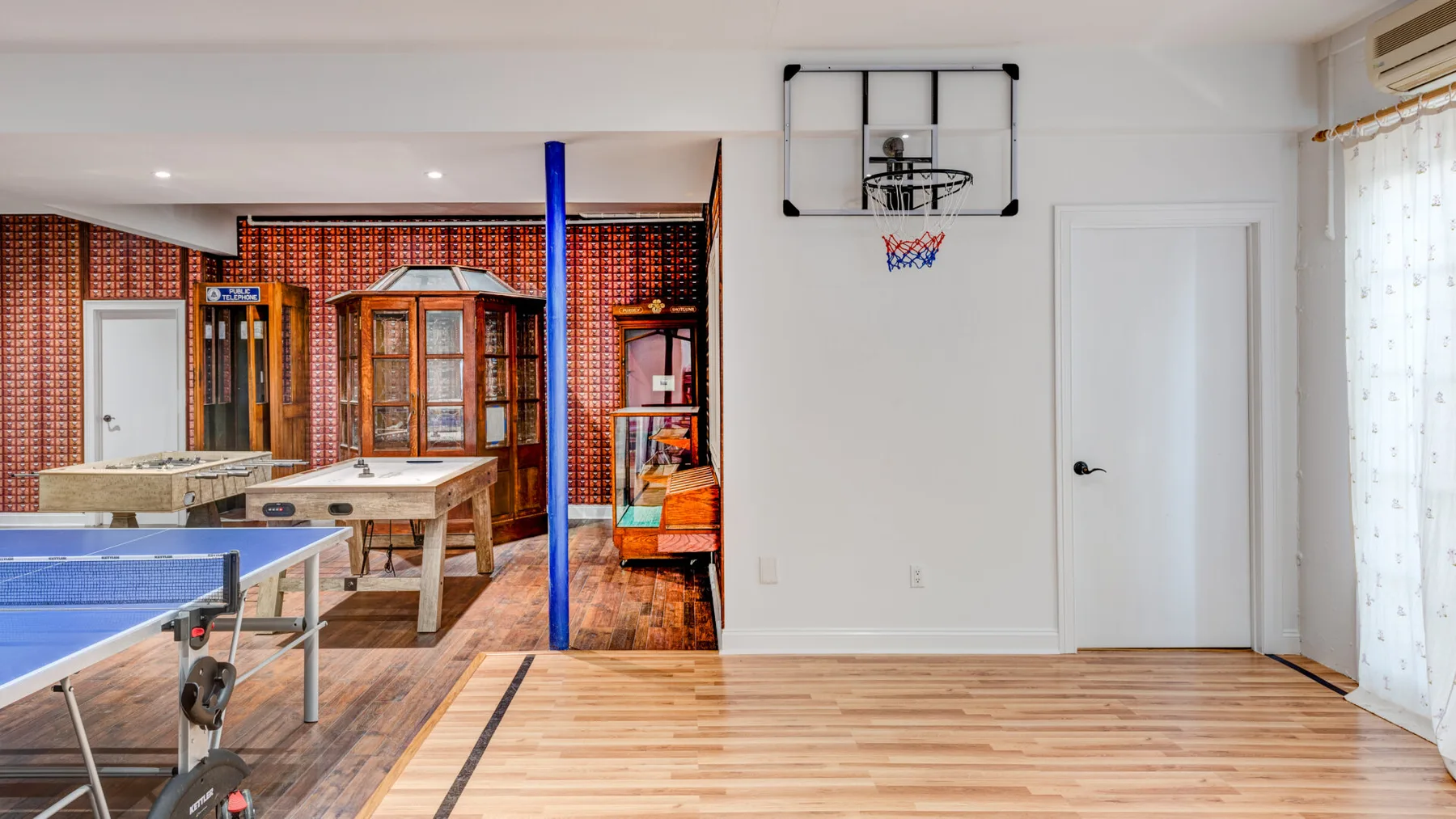 Una sala de juegos tiene una canasta de baloncesto, una mesa de ping-pong y mesas de juego.