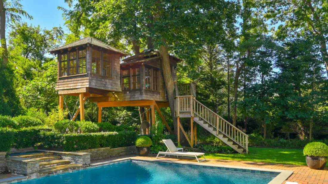 Una casa de árbol de madera se alza sobre una piscina en un jardín frondoso.