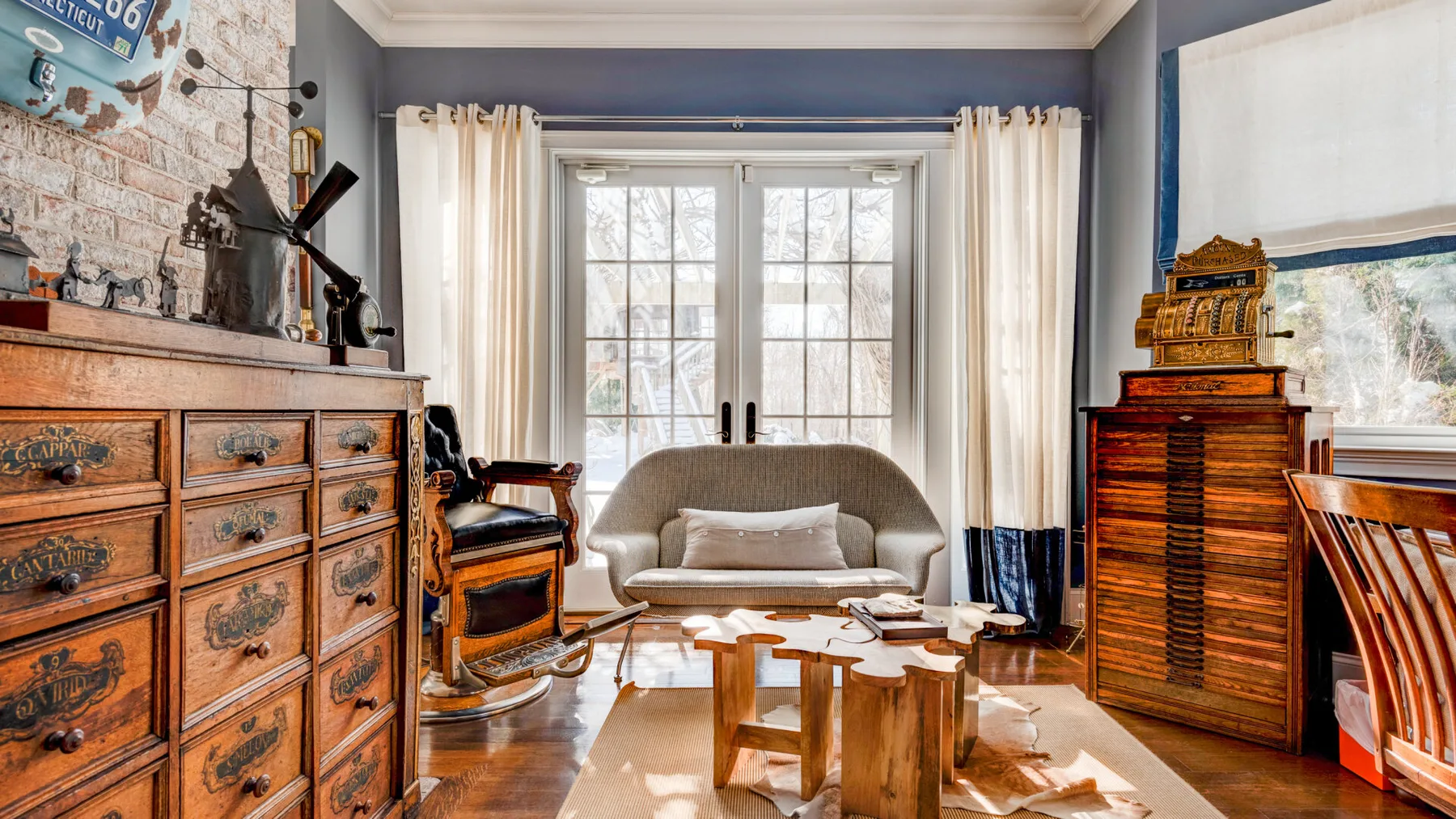 Una sala de estar con asientos y muebles de madera junto a ventanas altas.