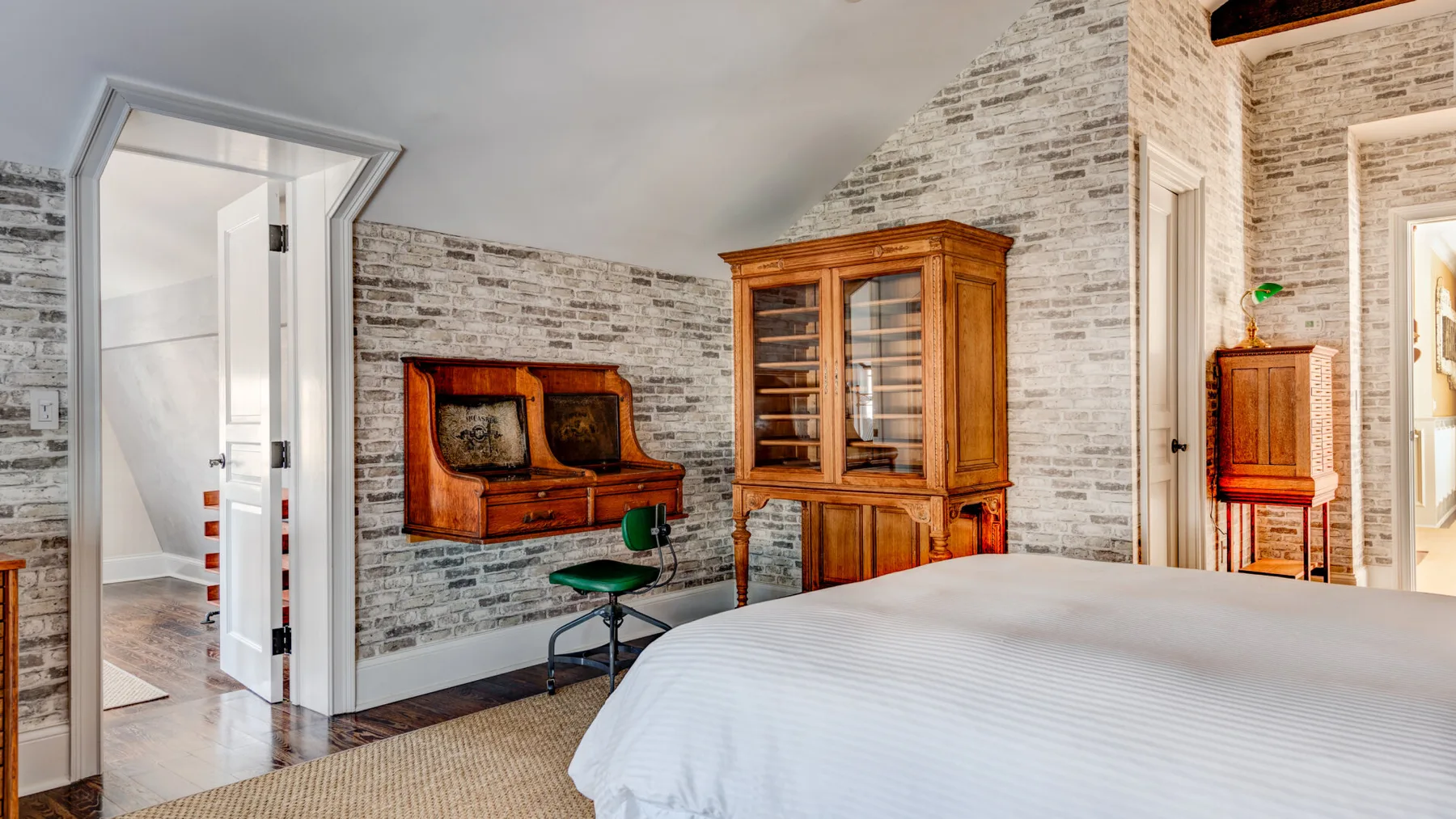 Dormitorio con cama blanca, mueble de madera y piano junto a paredes de diseño pétreo.