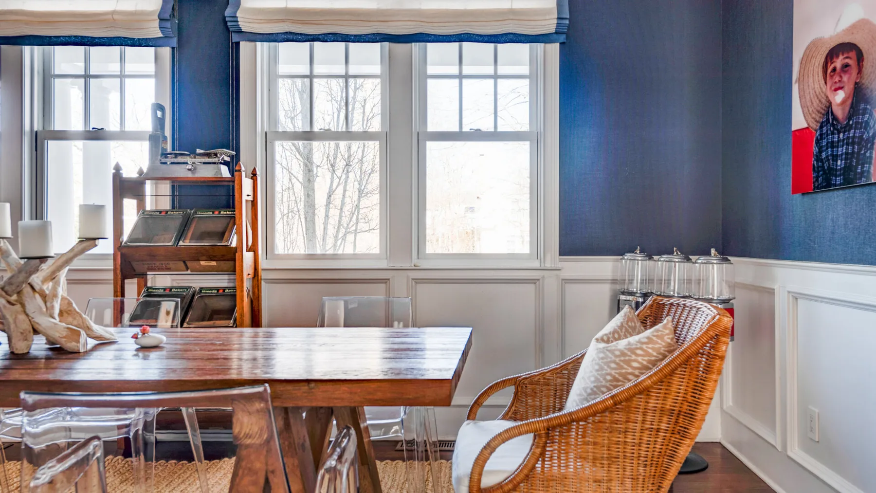 Comedor con una mesa de madera, asientos de mimbre y ventanas grandes.