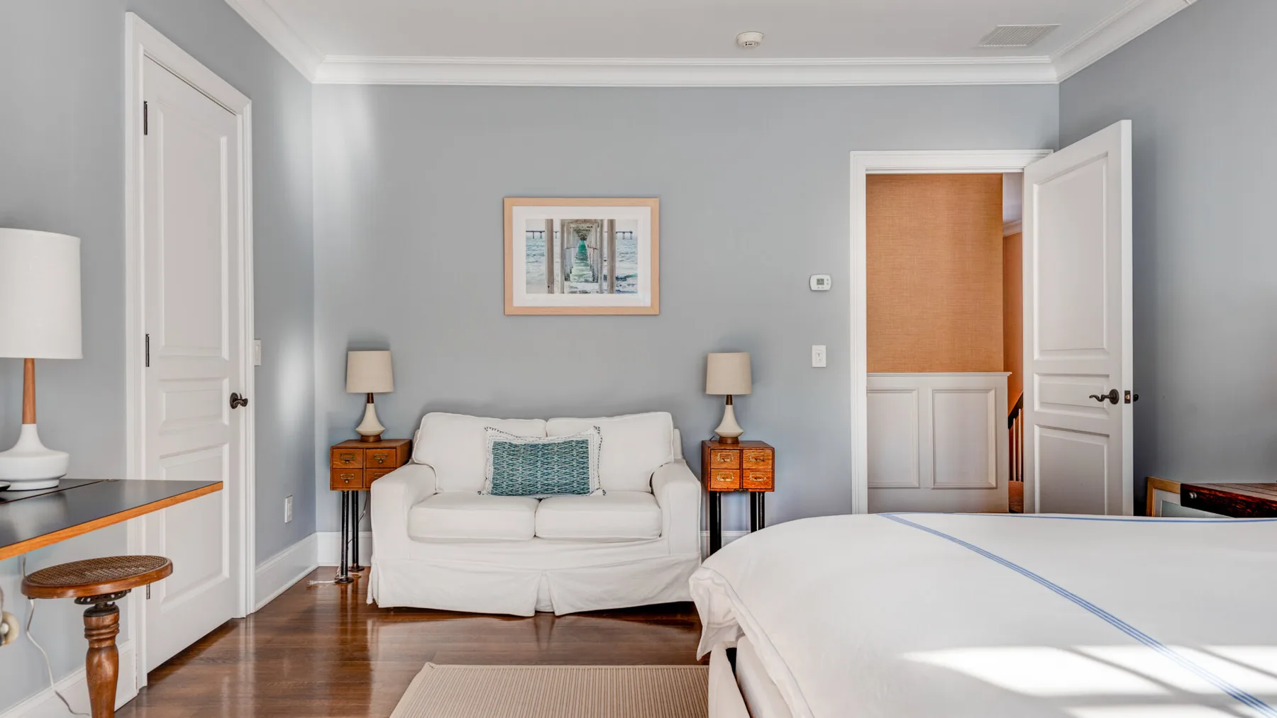 Un dormitorio con una cama blanca, un sofá y mesas auxiliares a juego.