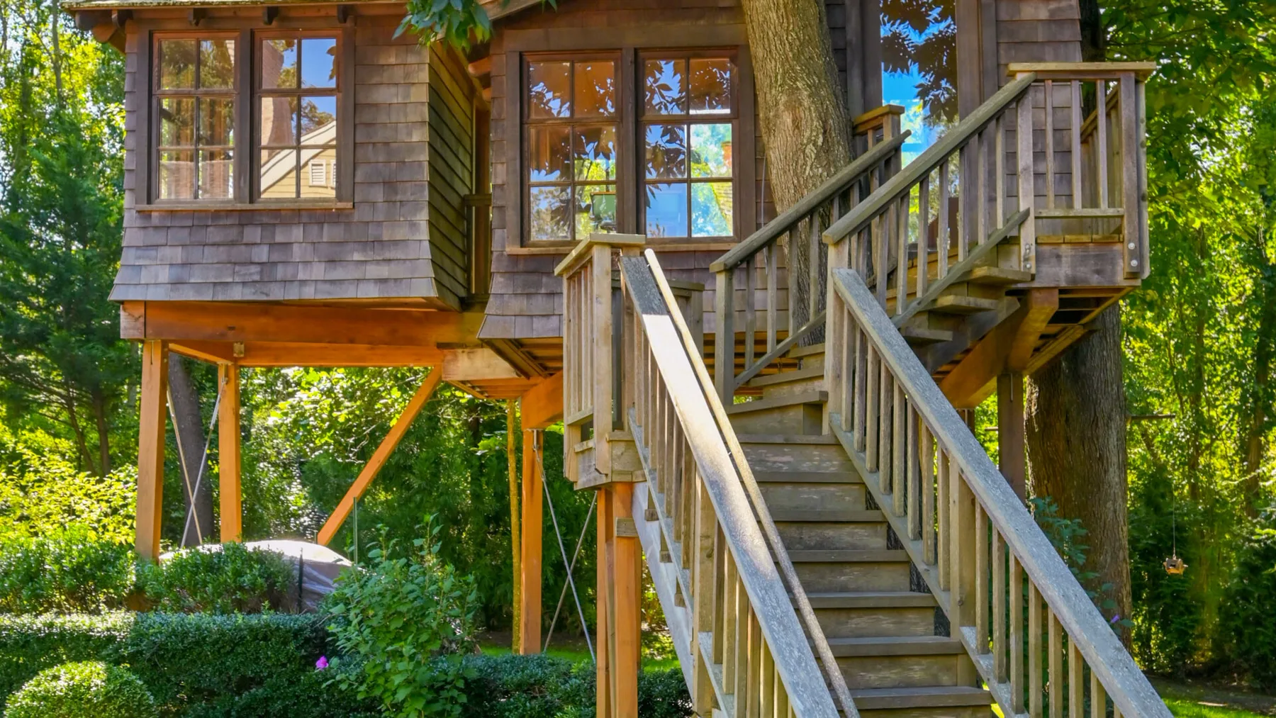 Una cabaña de madera elevada entre árboles, con una escalera exterior que lleva a su terraza.