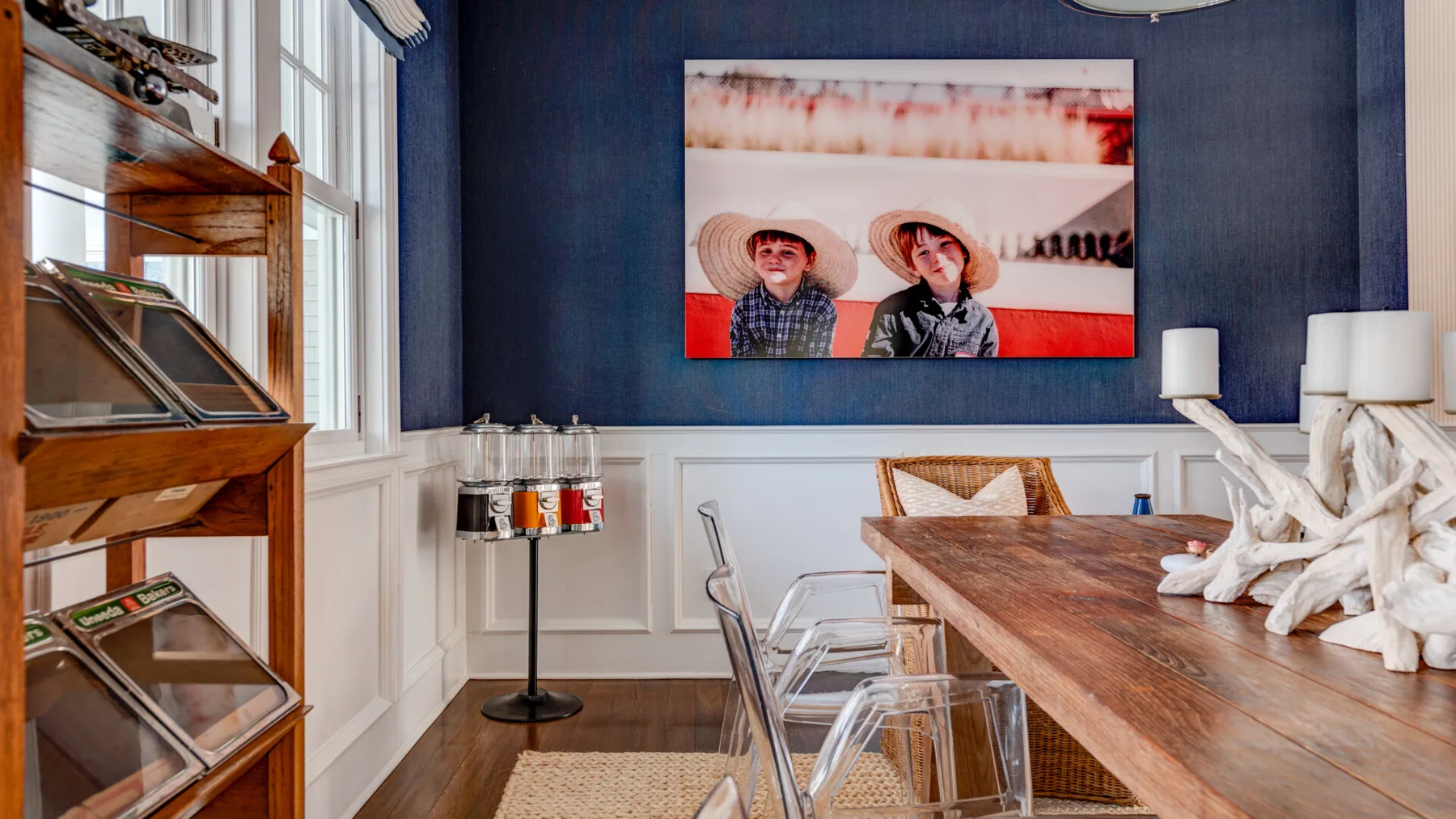 Comedor con una mesa larga de madera y una obra de arte en una pared azul oscuro.