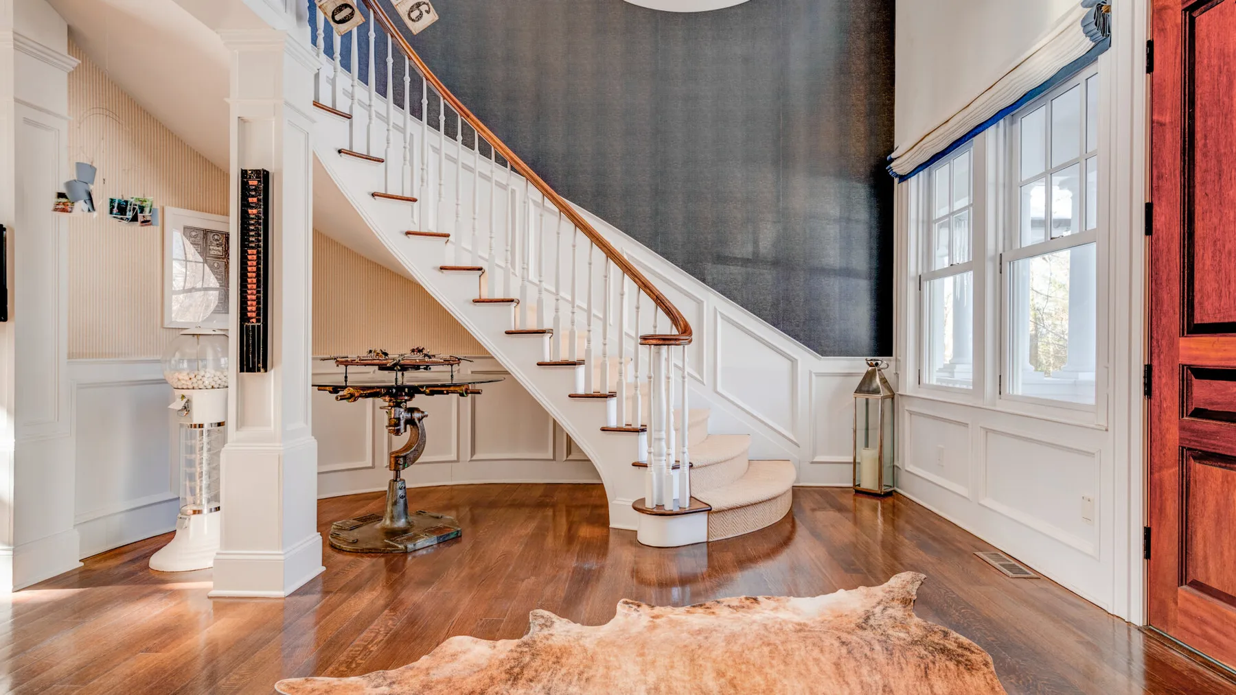 Un interior luminoso con una escalera junto a grandes ventanas y un suelo de madera.