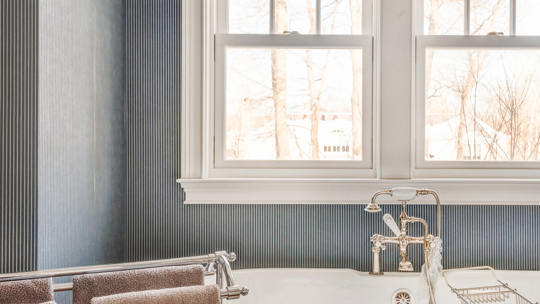 Un tocador de baño con grifo está bajo unas ventanas luminosas.
