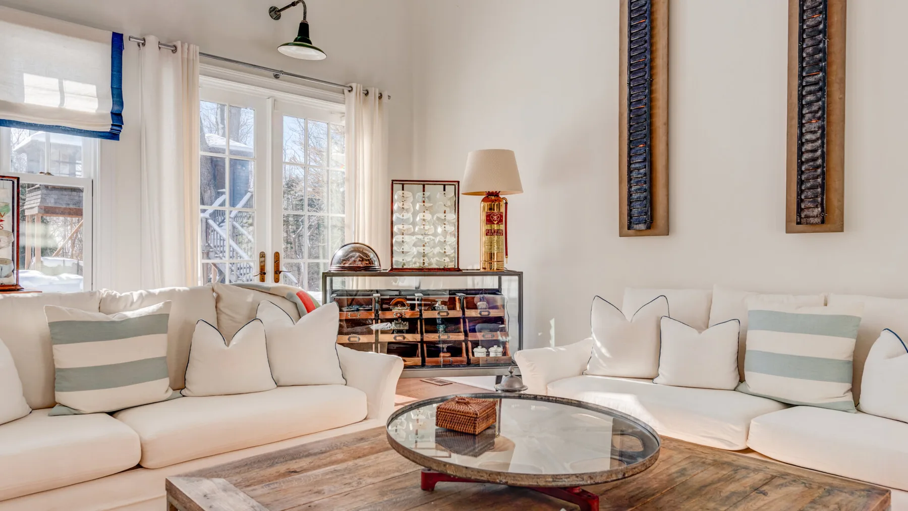 Una sala luminosa con asientos blancos, una mesa de centro de vidrio y ventanas grandes.
