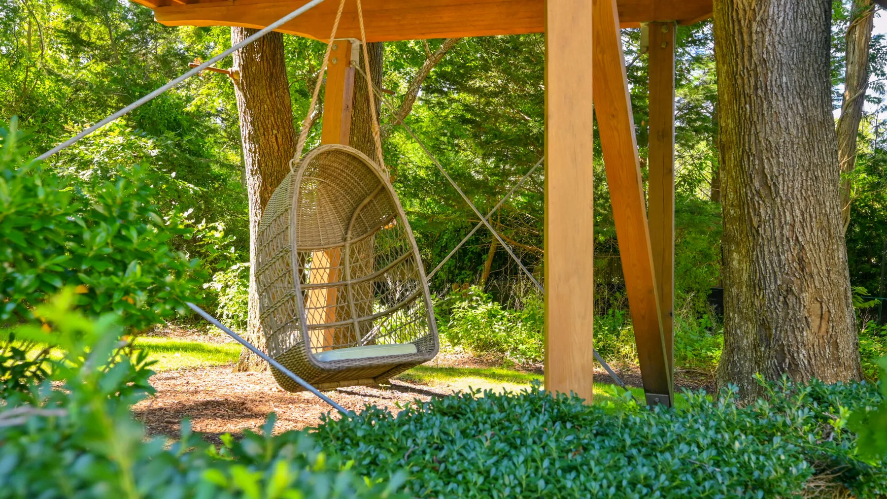 Un asiento colgante bajo un refugio de madera en un jardín frondoso.