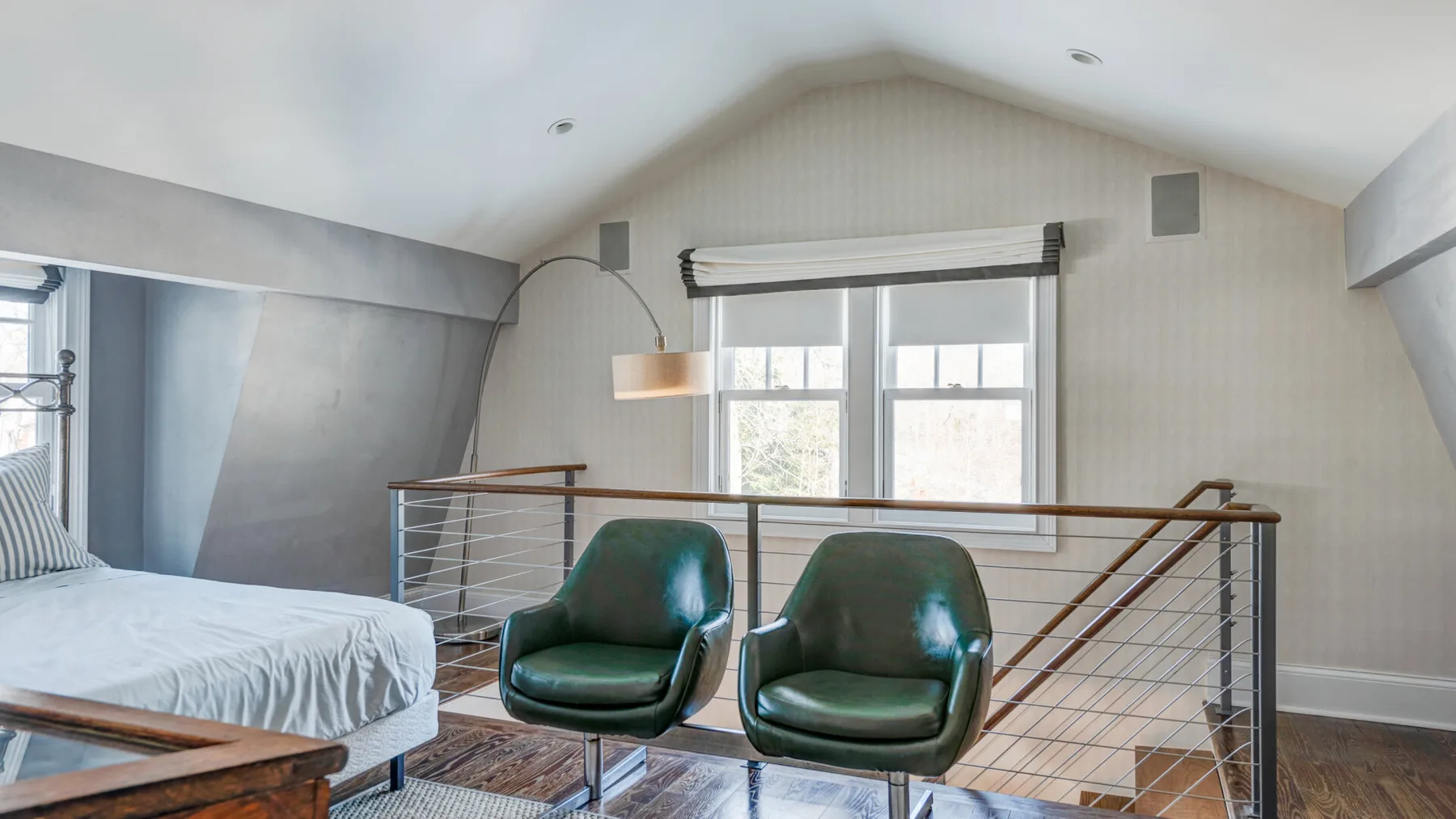 Un dormitorio tipo loft luminoso tiene una cama y dos sillones verdes junto a una barandilla.