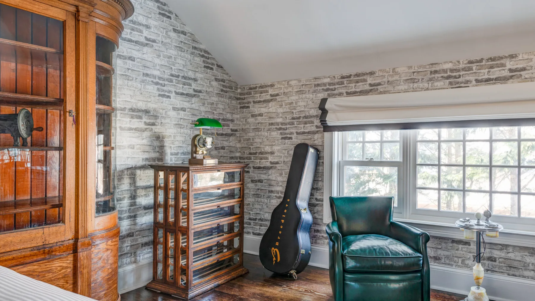 Una habitación luminosa con un sillón de cuero, una guitarra y grandes ventanas.