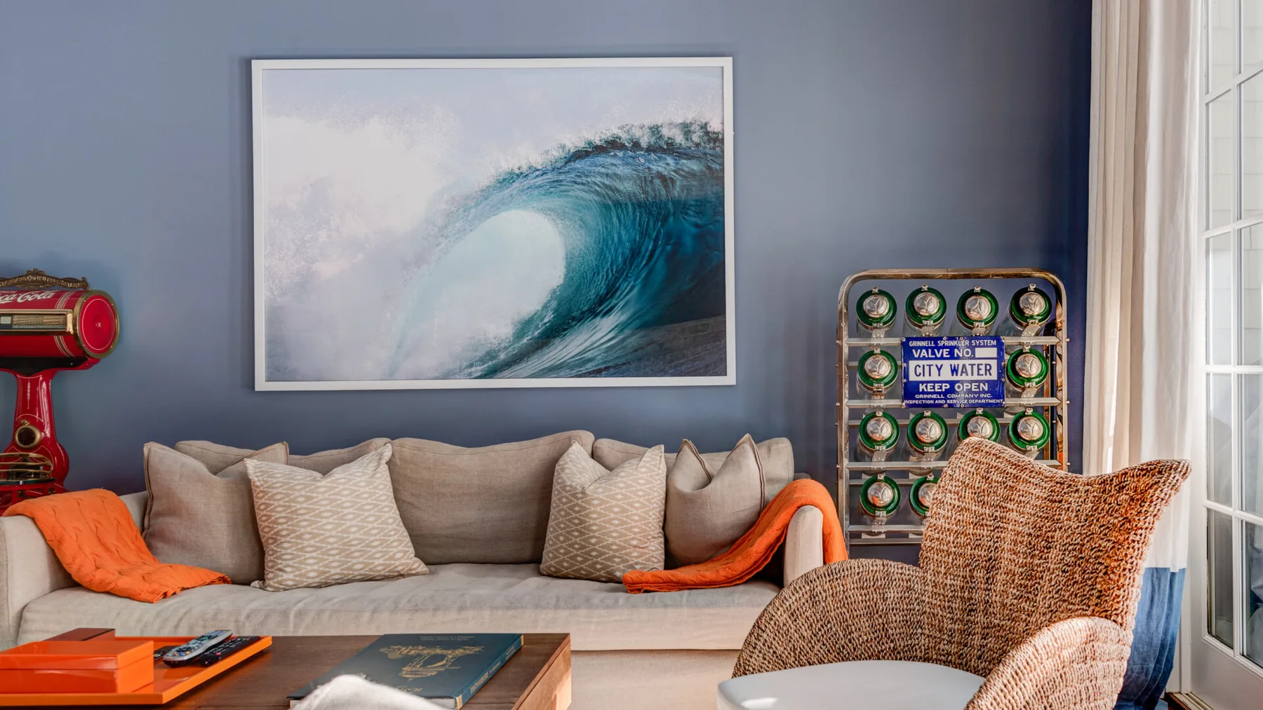 Una sala de estar con un sofá, una silla tejida y una imagen enmarcada de una ola.