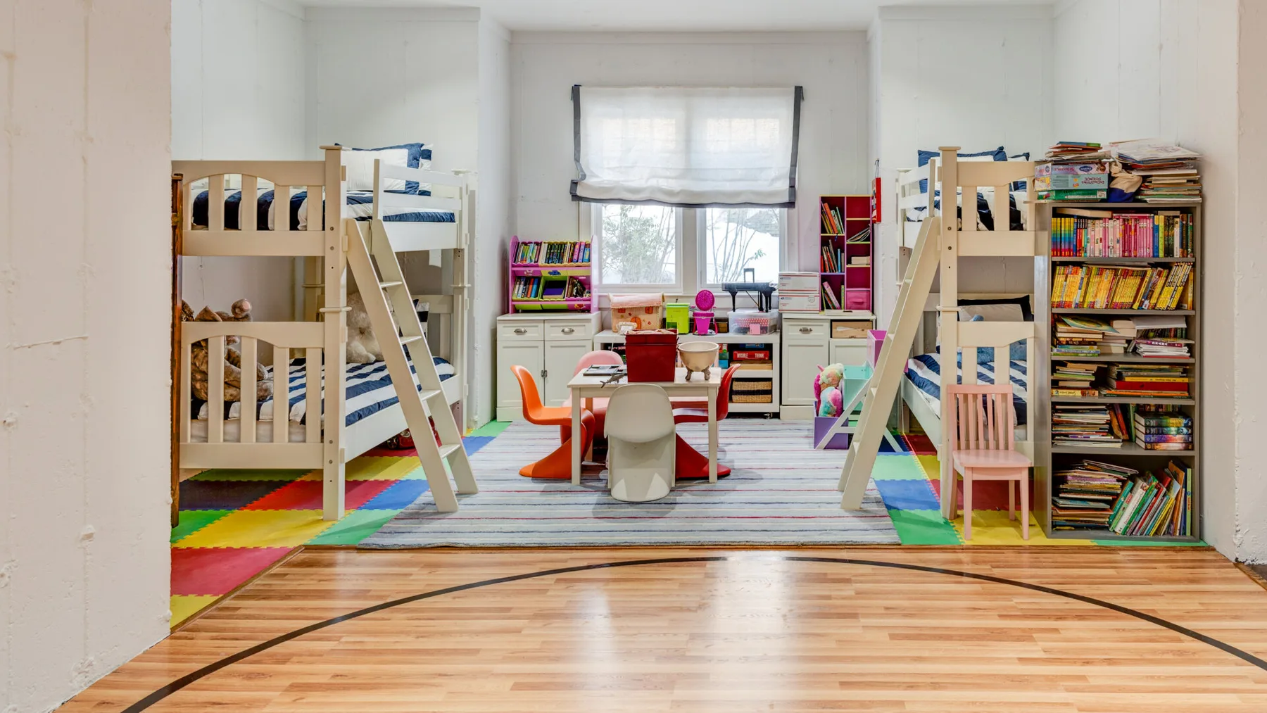 Un colorido cuarto de juegos infantil con literas, estanterías de libros y una mesa pequeña.