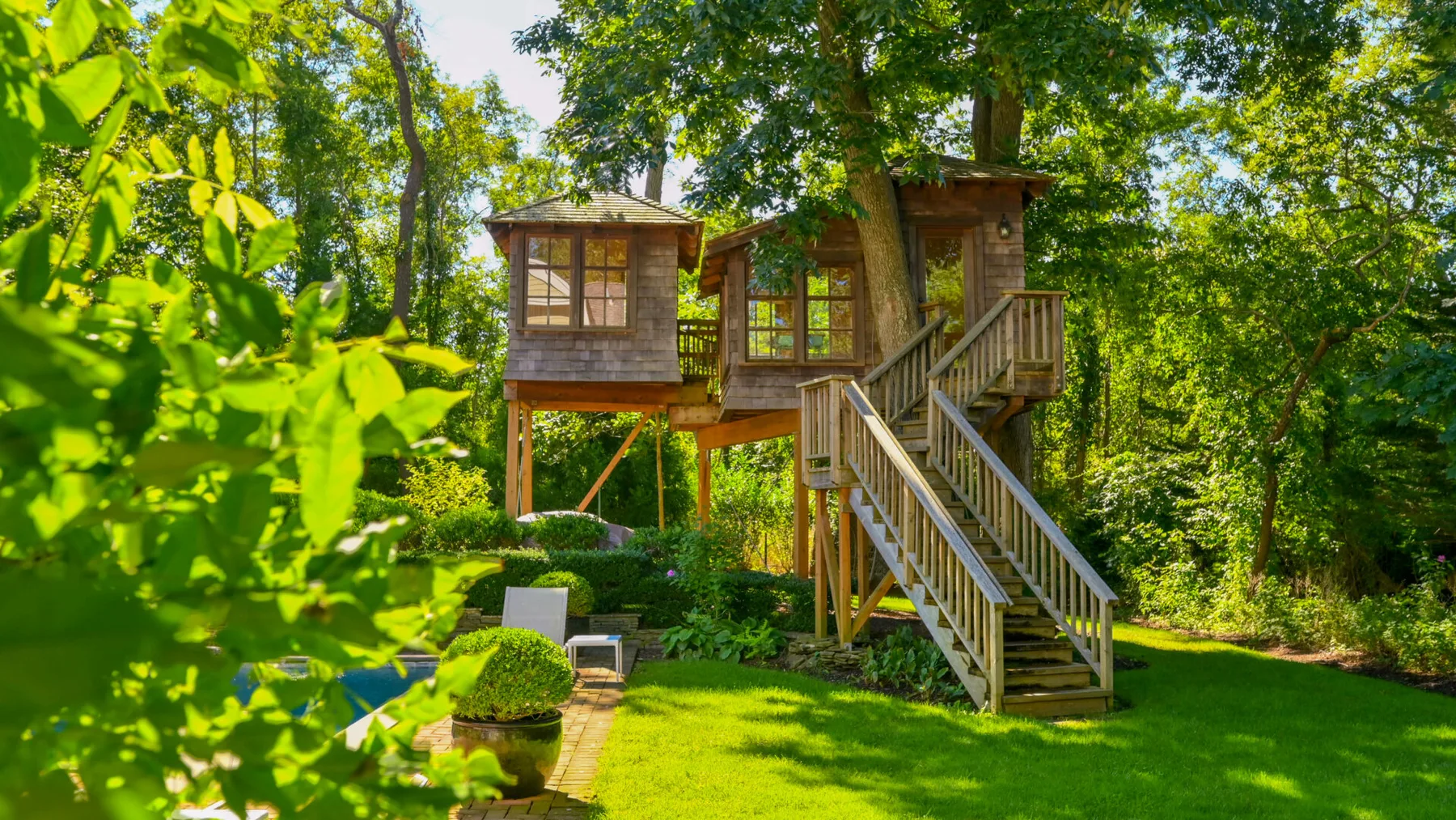 Una casa de árbol de madera se alza entre árboles frondosos sobre un césped verde.