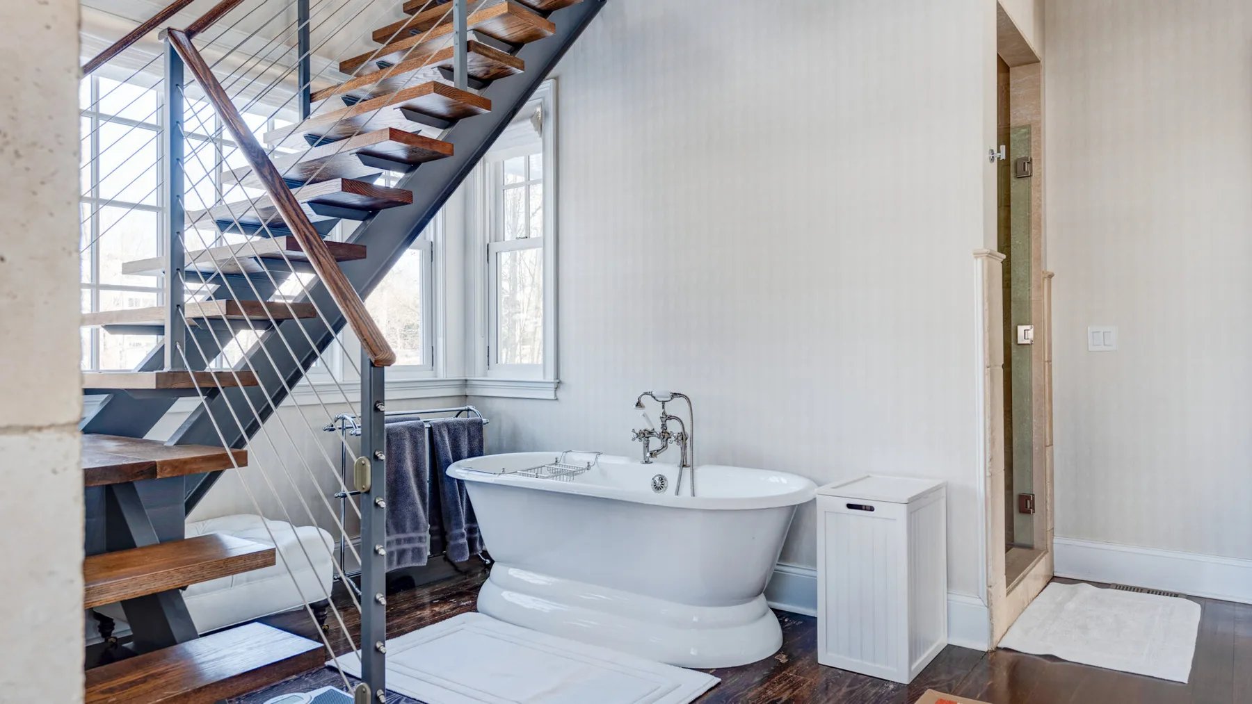 Un baño luminoso con una bañera exenta bajo una escalera abierta.