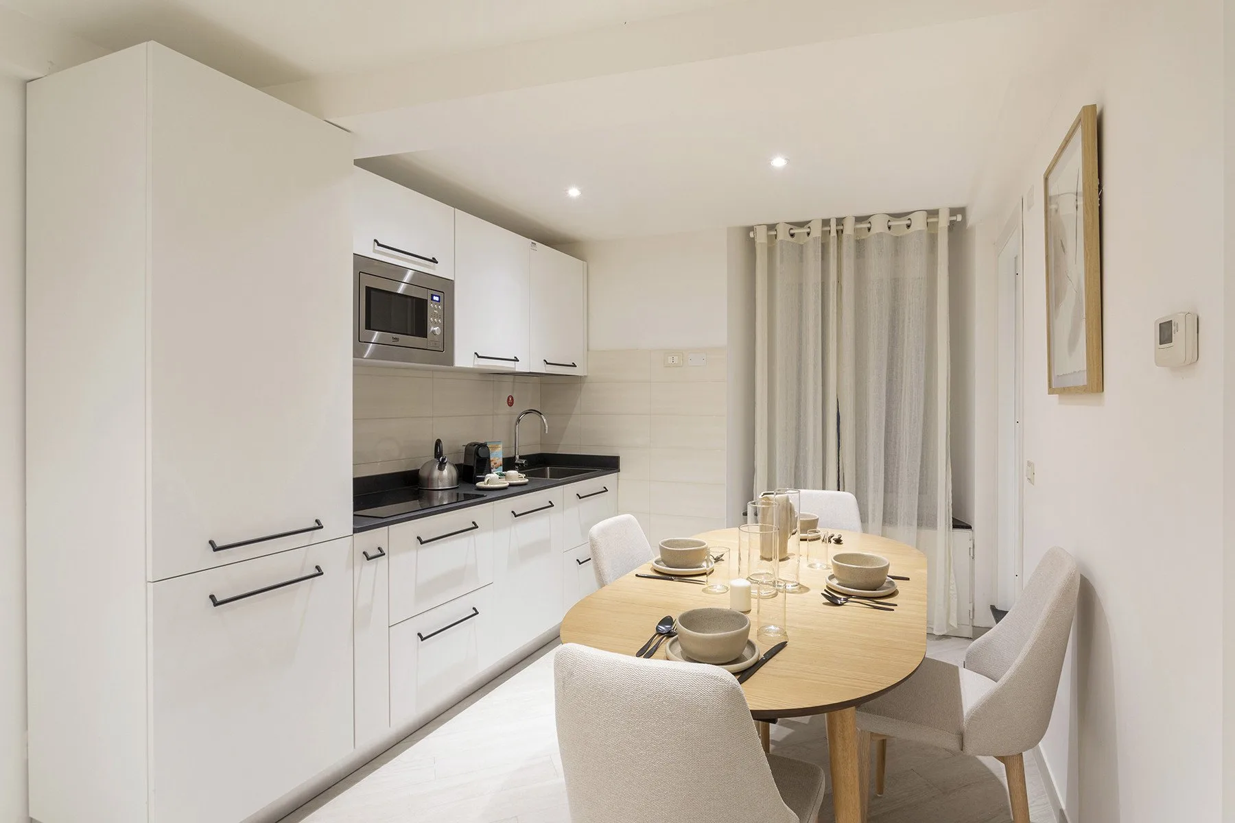 Una cocina y zona de comedor luminosa, con armarios blancos y una mesa ovalada.