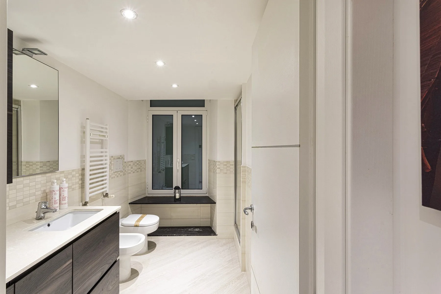 Un baño luminoso con un tocador largo, espejo de pared y bañera bajo la ventana.
