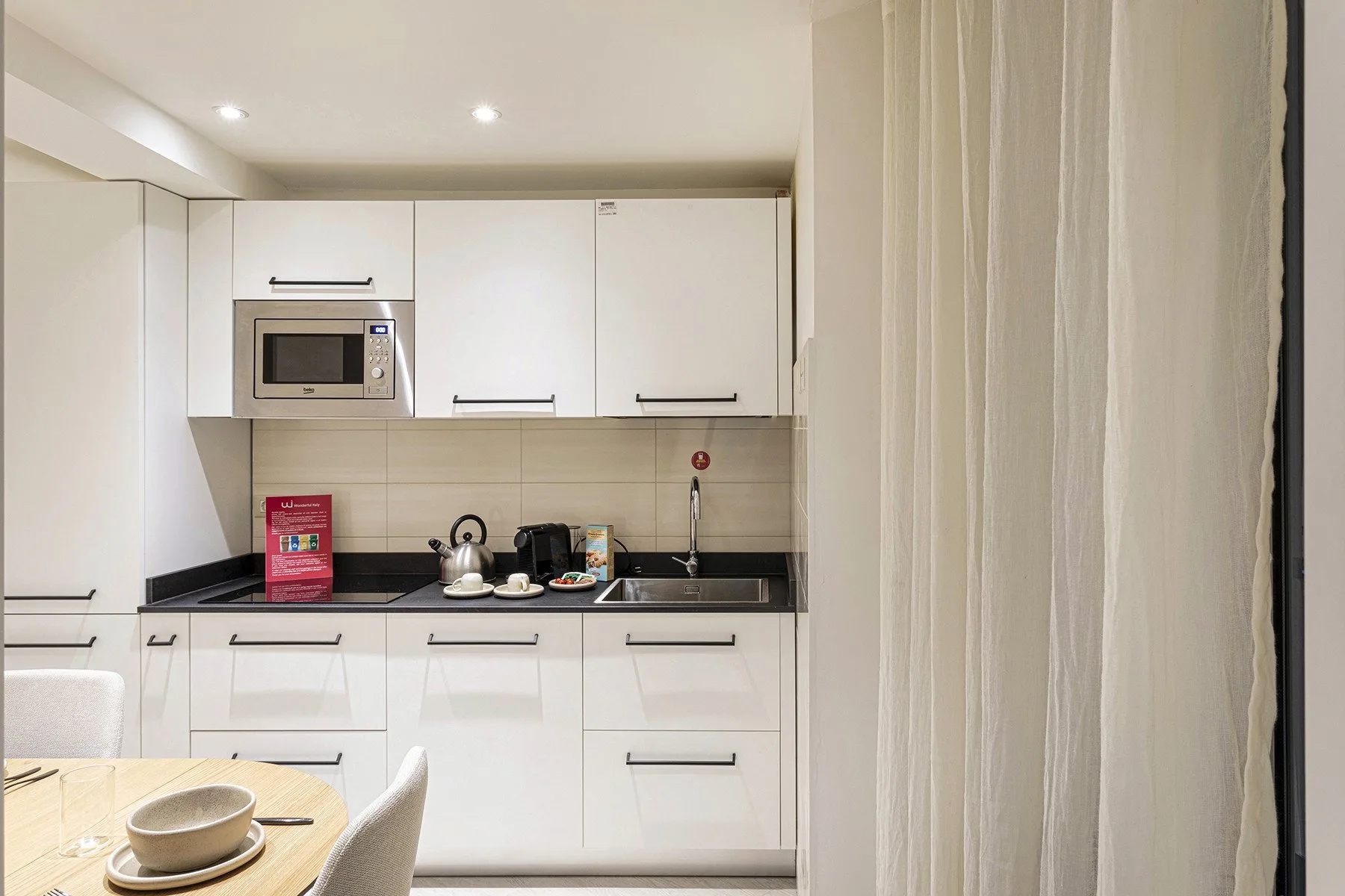 Una cocina compacta con gabinetes blancos, una encimera y una mesa de comedor en primer plano.