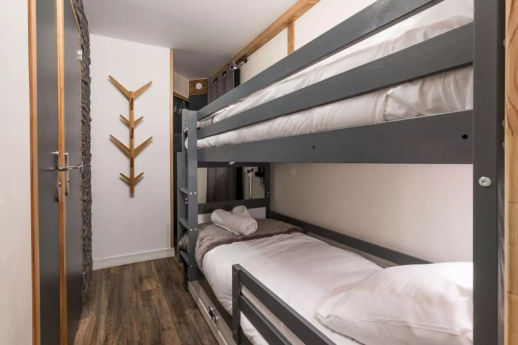 Una litera ocupa un dormitorio compacto con suelo de aspecto madera.