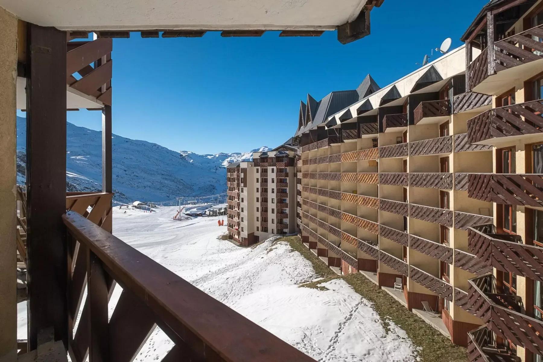 Un balcón de madera da a montañas nevadas y edificios de apartamentos cercanos.
