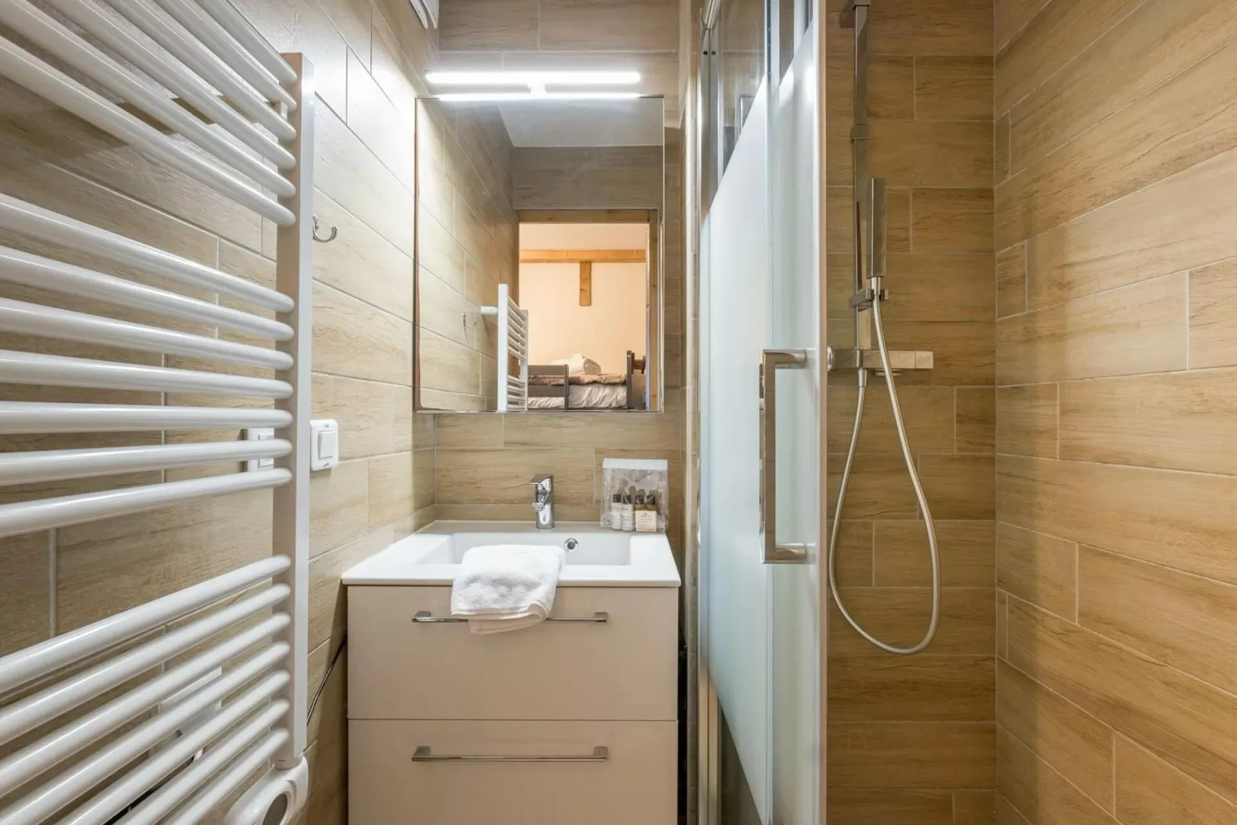 Un baño revestido de azulejos con lavabo, espejo y ducha de cristal.