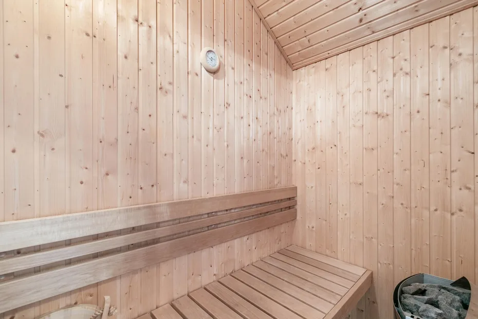 Una sauna revestida de madera con asientos escalonados y un pequeño calentador de piedras.