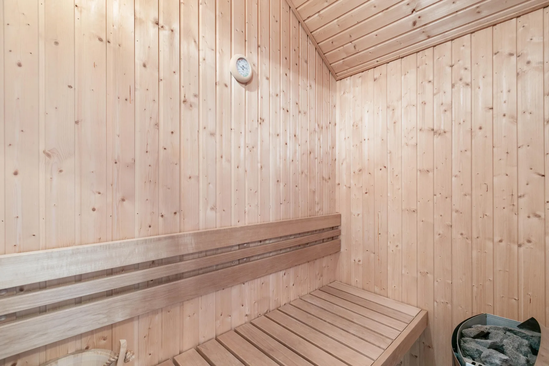 Una sauna de madera con asientos escalonados y un cubo de piedras.