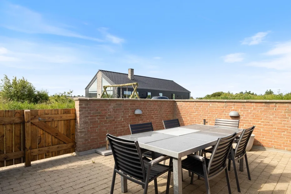 Una zona de comedor exterior pavimentada con mesa y asientos junto a un muro de ladrillo.