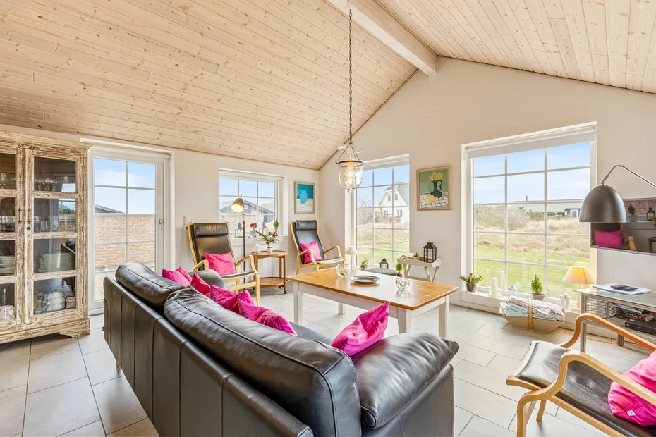 A bright living room with a dark sofa, colorful cushions, and large windows.