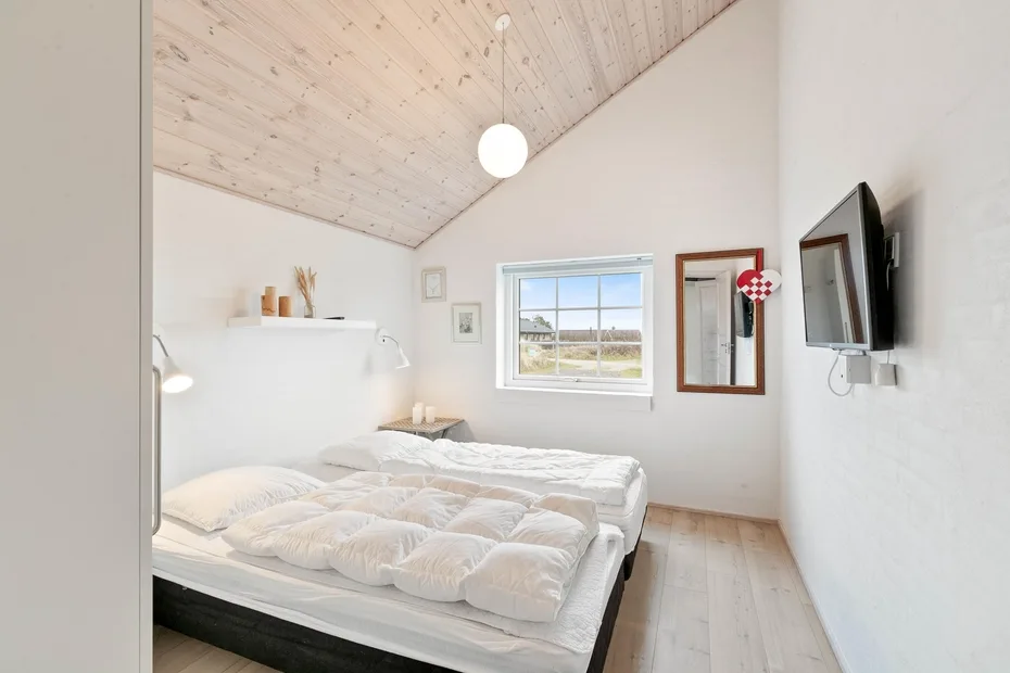 Un dormitorio luminoso con camas bajo un techo inclinado revestido de madera.