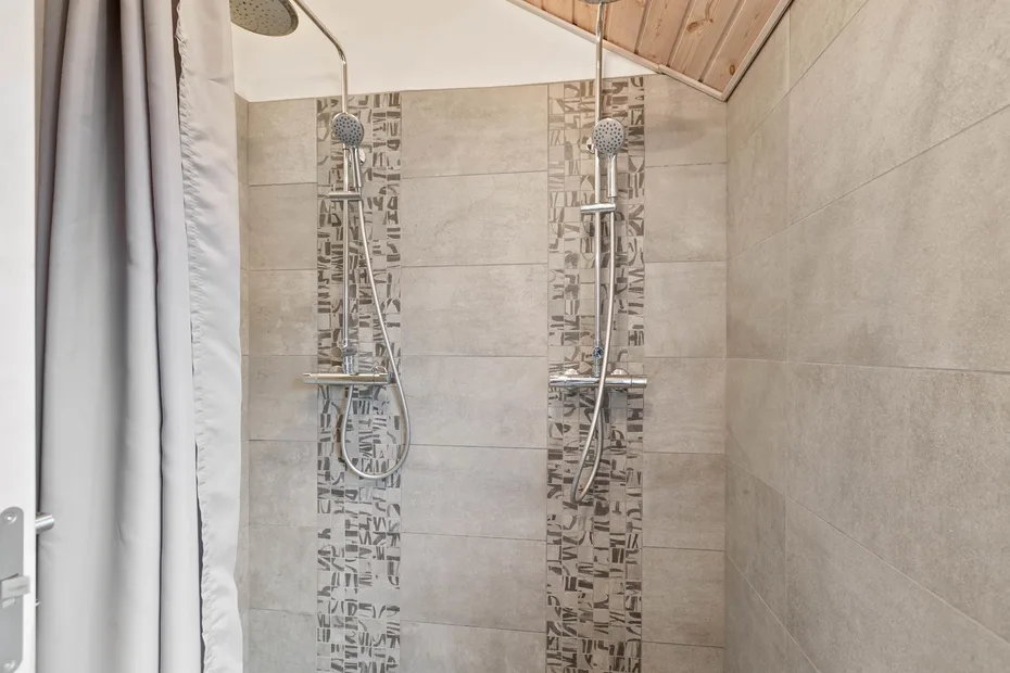 Zona de ducha con azulejos, dos duchas y una cortina.
